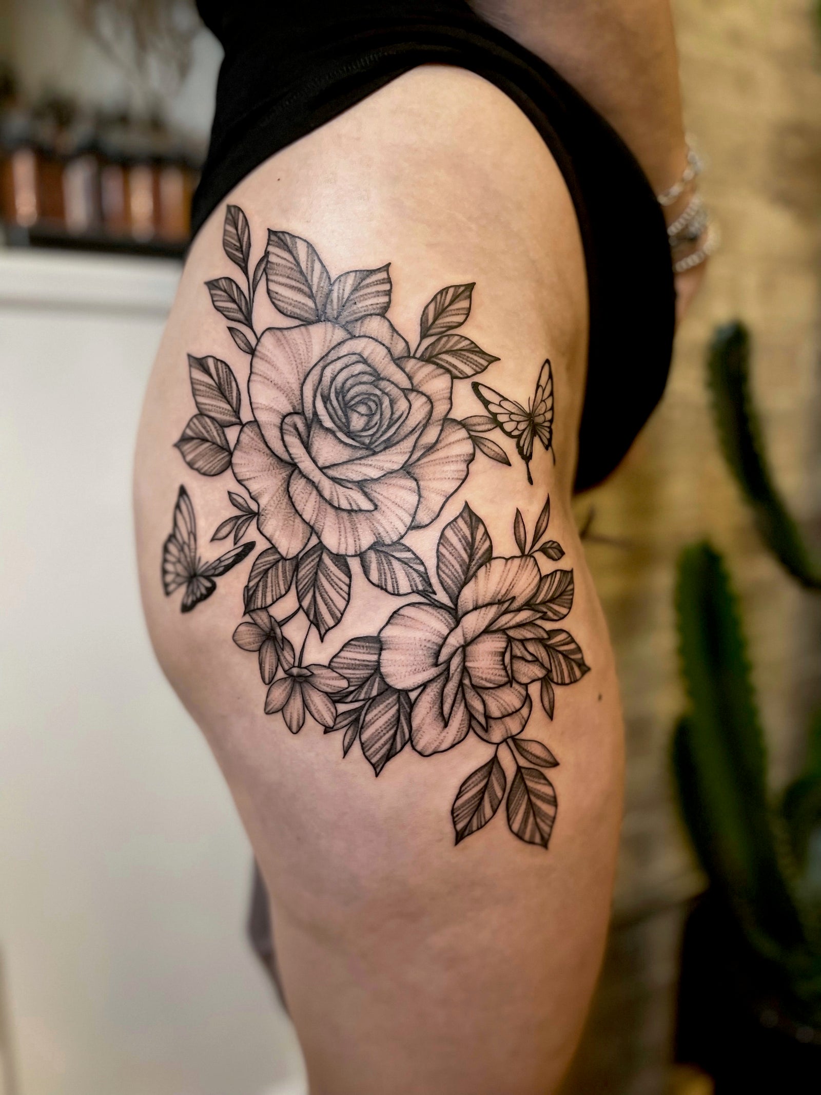 Delicate, black work floral rose hip and thigh tattoo by Janice Danger
