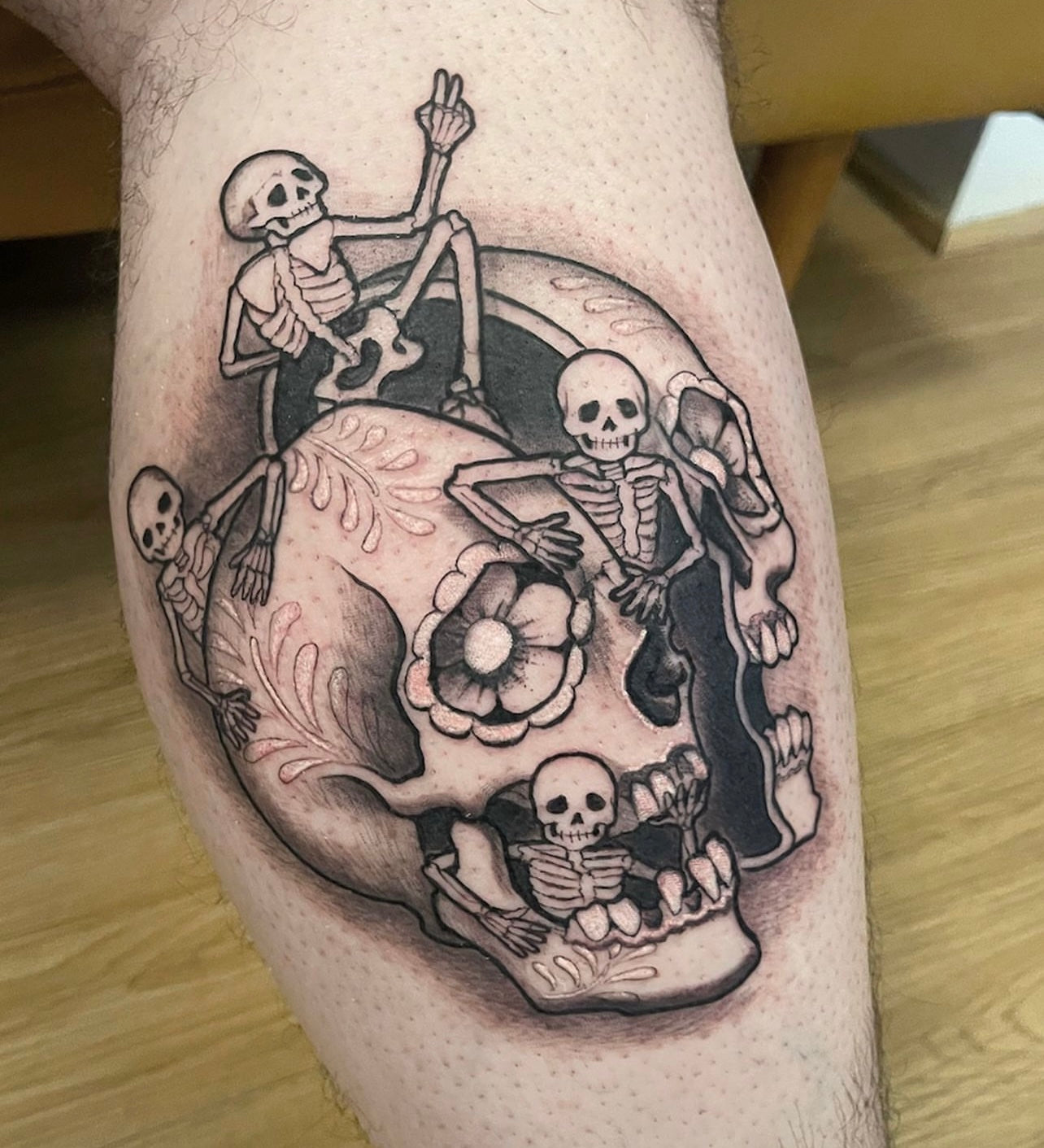 Black and gray skull with skeletons calf tattoo by Elvia Guadian at Grit N Glory in New York City