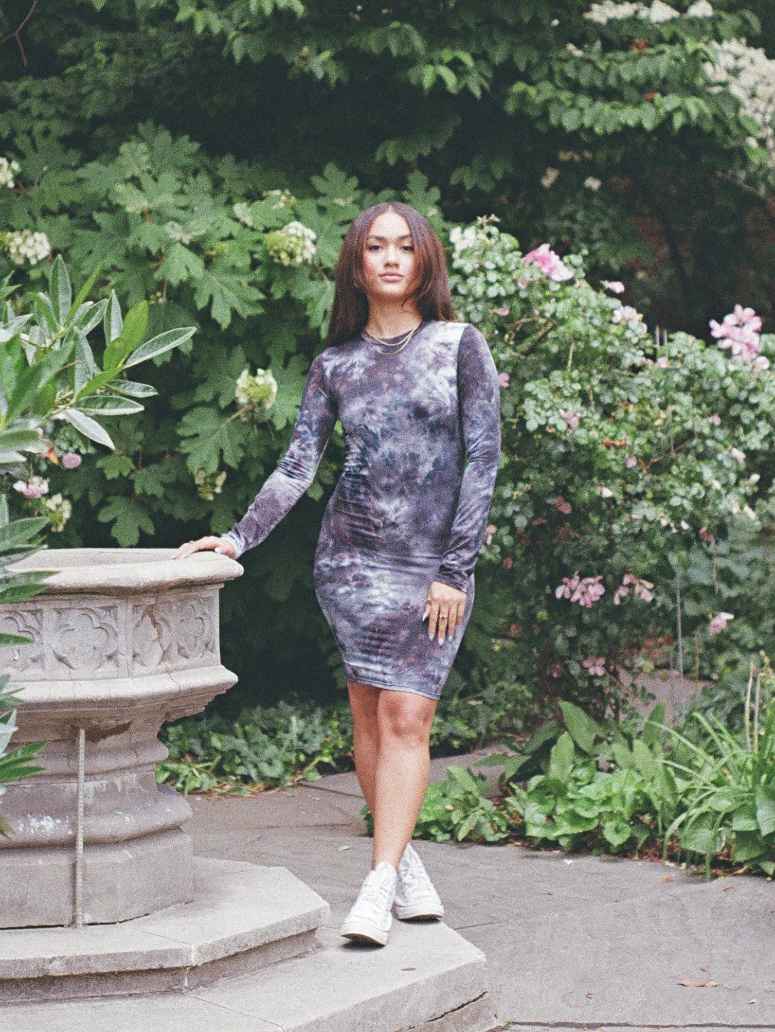 Model wearing a long sleeved, cool toned, tie dyed midi dress in a floral garden.