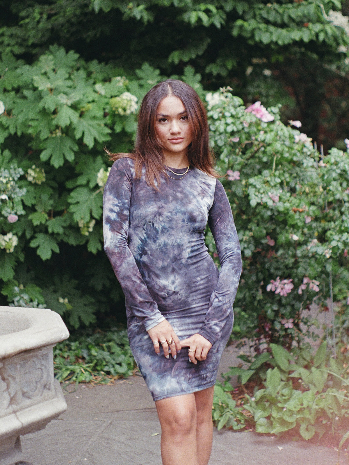 Model wearing a long sleeved, cool toned, tie dyed midi dress in a floral garden.