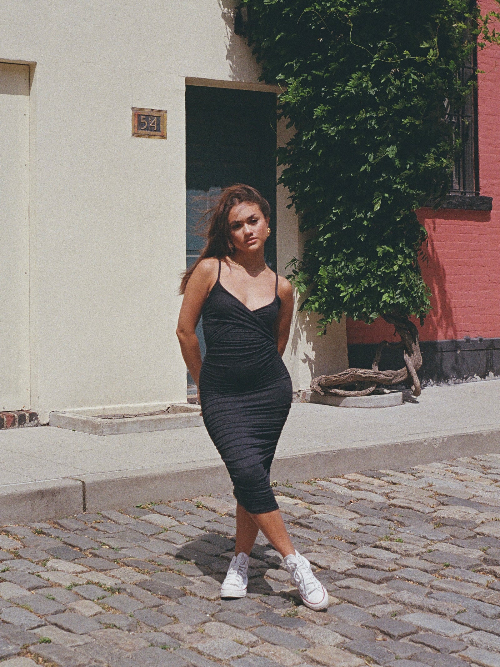 Model wearing a spaghetti strapped black midi dress with white converse sneakers on a cobblestone street