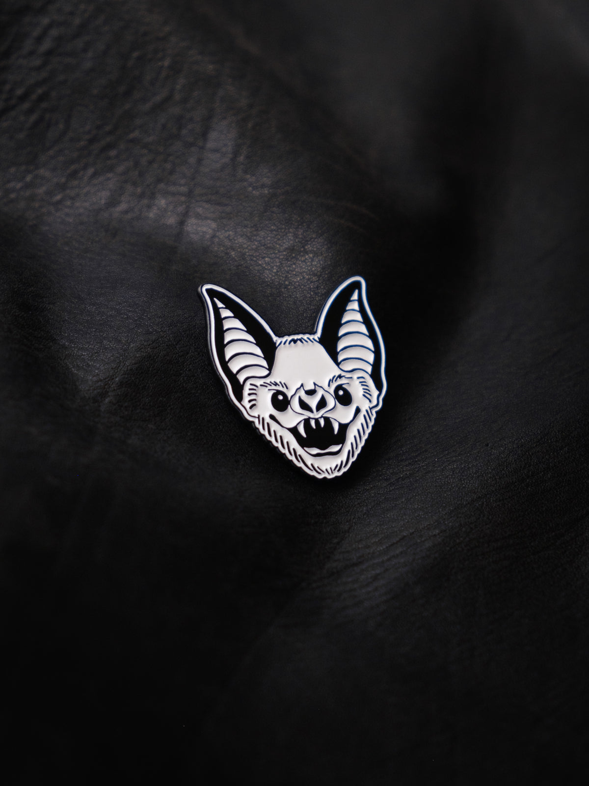 A black and white enamel pin with a bat design.