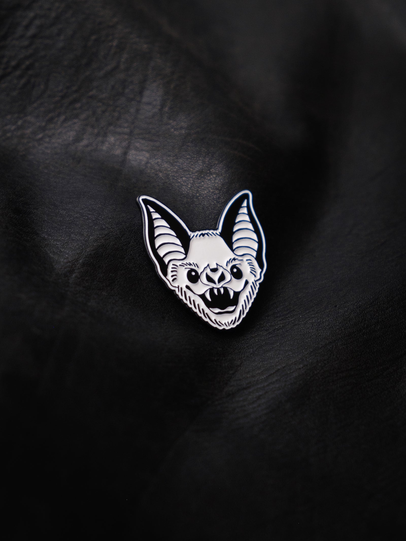 A black and white enamel pin with a bat design.