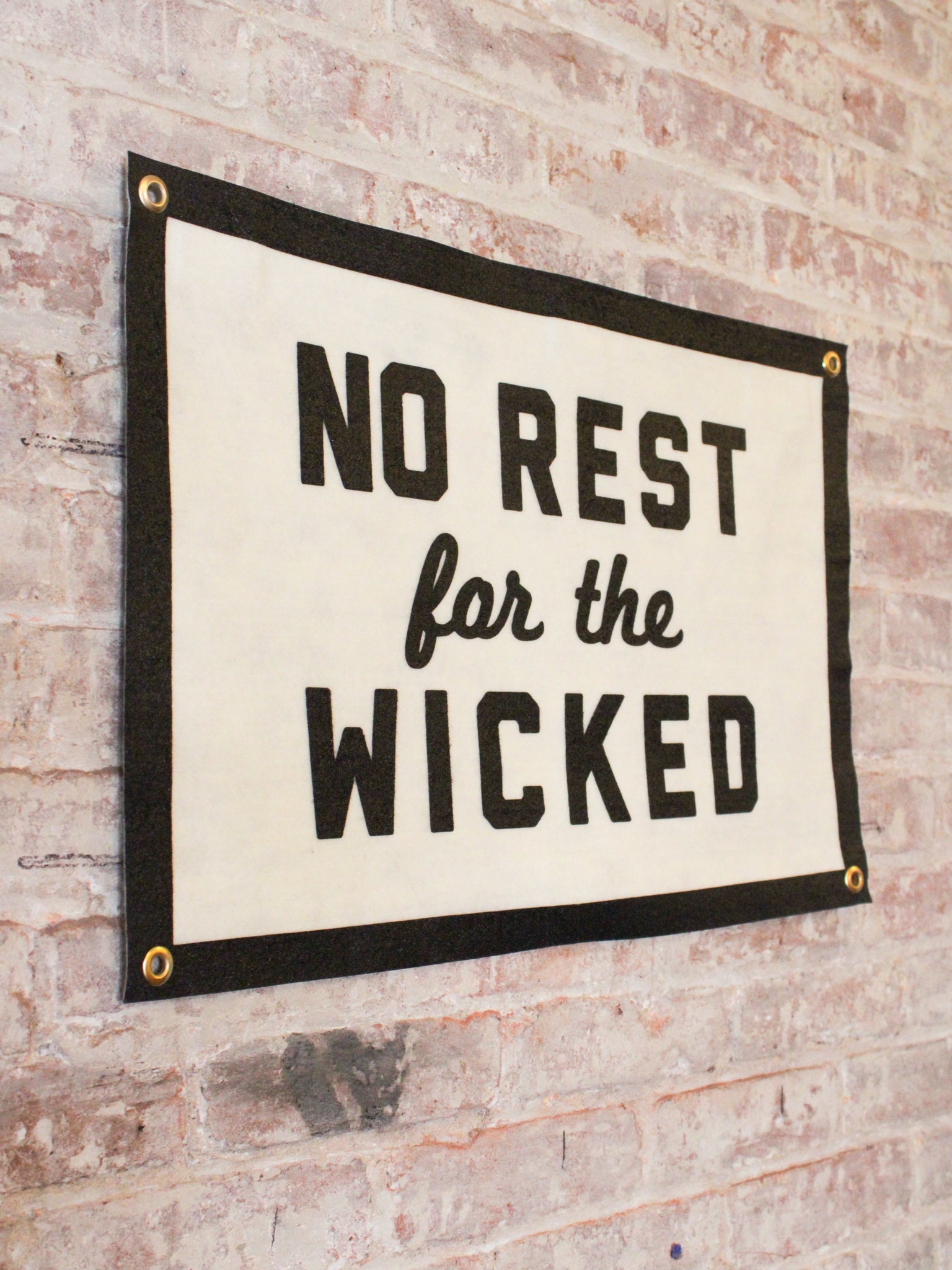 off white and black banner reads "No Rest for the Wicked" with gold grommets