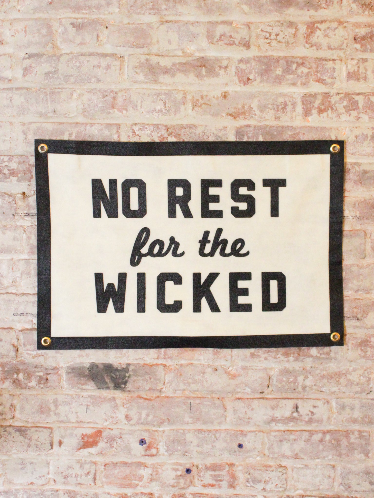 off white and black banner reads "No Rest for the Wicked" with gold grommets
