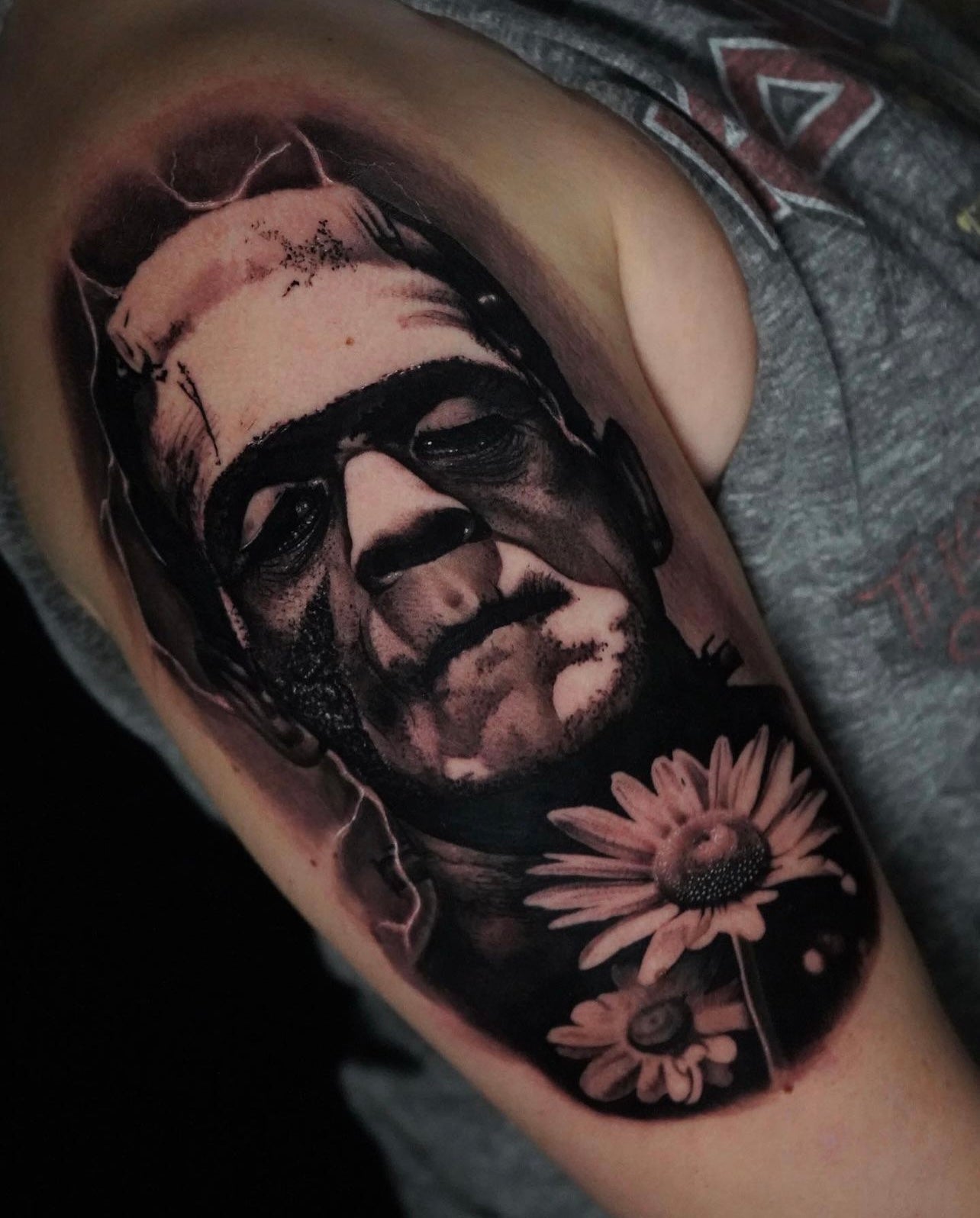 Black and gray upper arm tattoo of Frankenstein's monster with daisies made by Joanna Gacek