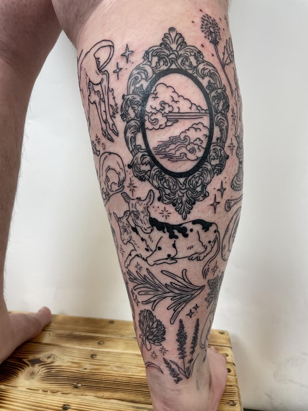 blackwork patchwork leg tattoo with cow, foliage, ornate frame by Mehak Basu