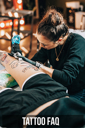 Photograph of Janice Danger tattooing a laurel on a knee at Grit N Glory. Button reads Tattoo FAQ