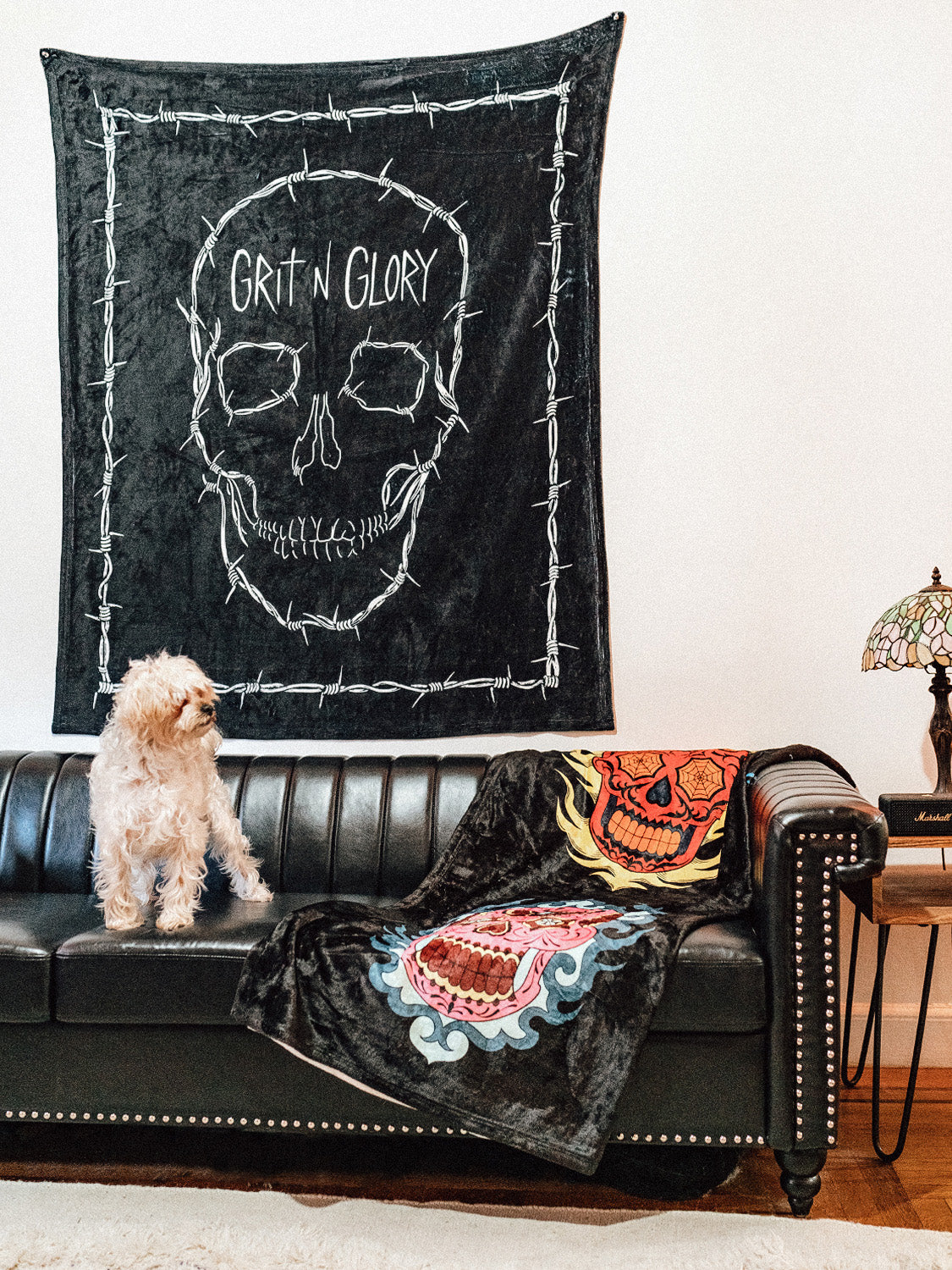 A black blanket with a white skull design and the text 'GRIT N GLORY' on a wall, likely used as a decorative piece.