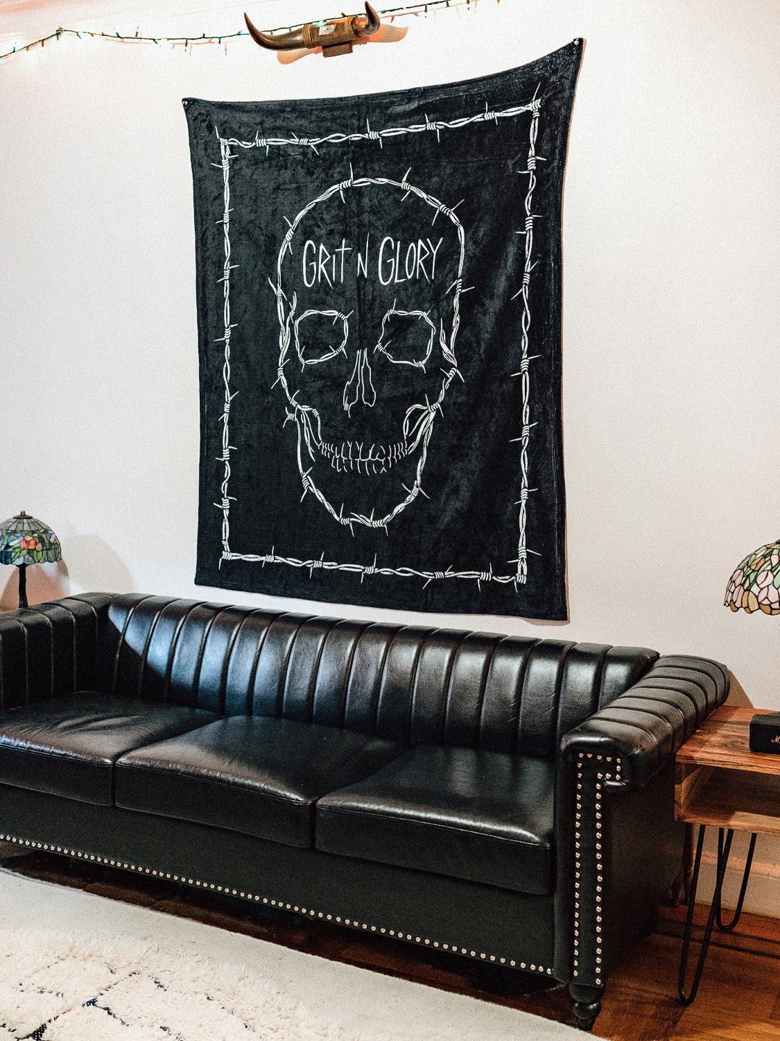 A black blanket with a white skull design and the text 'GRIT N GLORY' on a wall, likely used as a decorative piece.