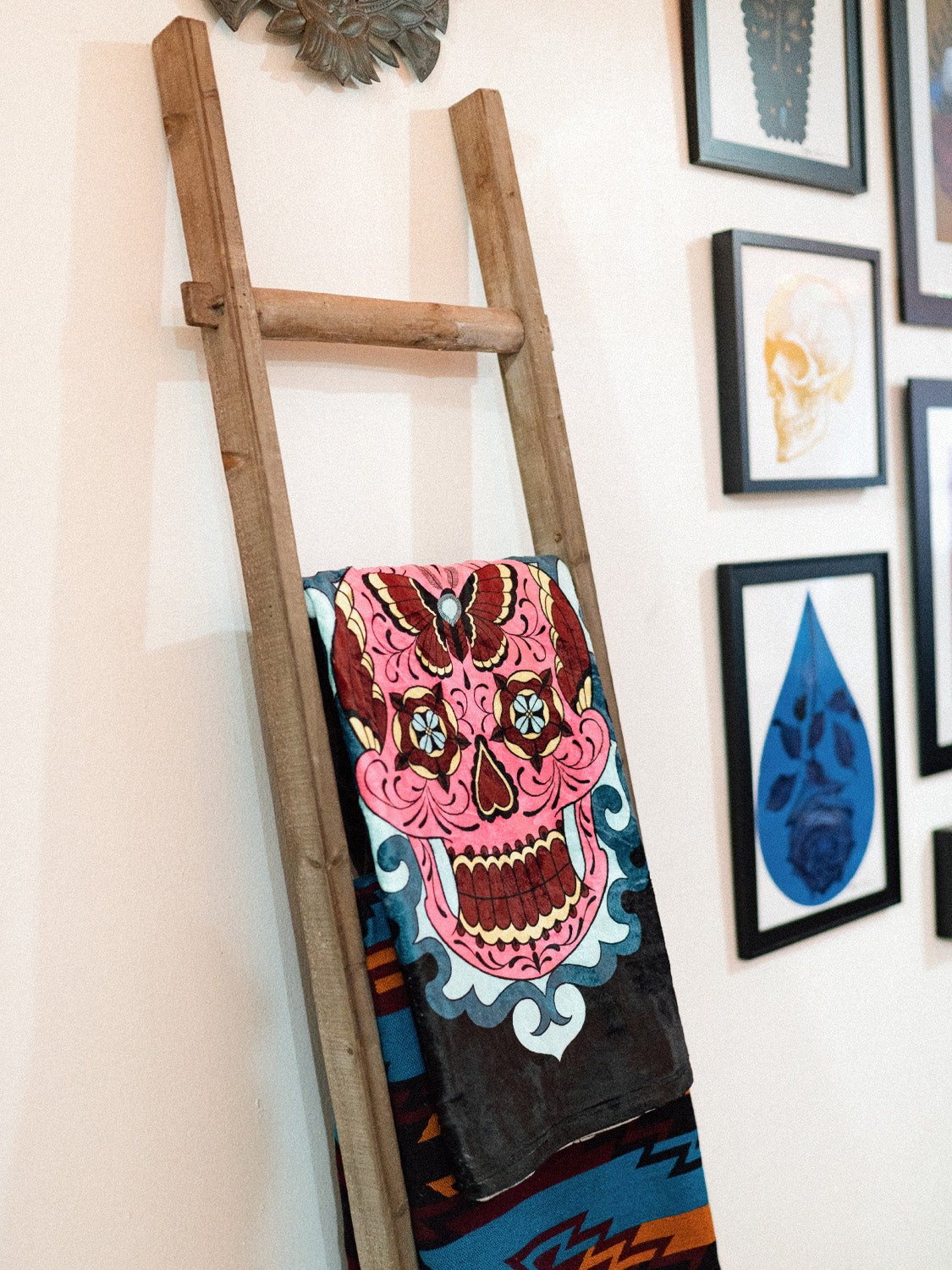 A black and white plush blanket with a colorful sugar skull design displayed on a decorative ladder.