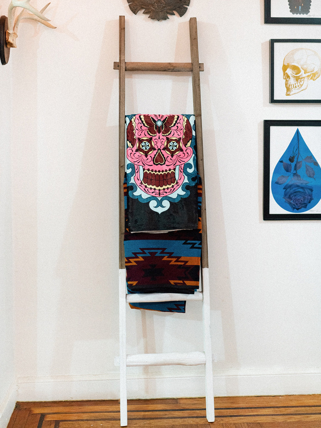 A black and white plush blanket with a colorful sugar skull design displayed on a decorative ladder.