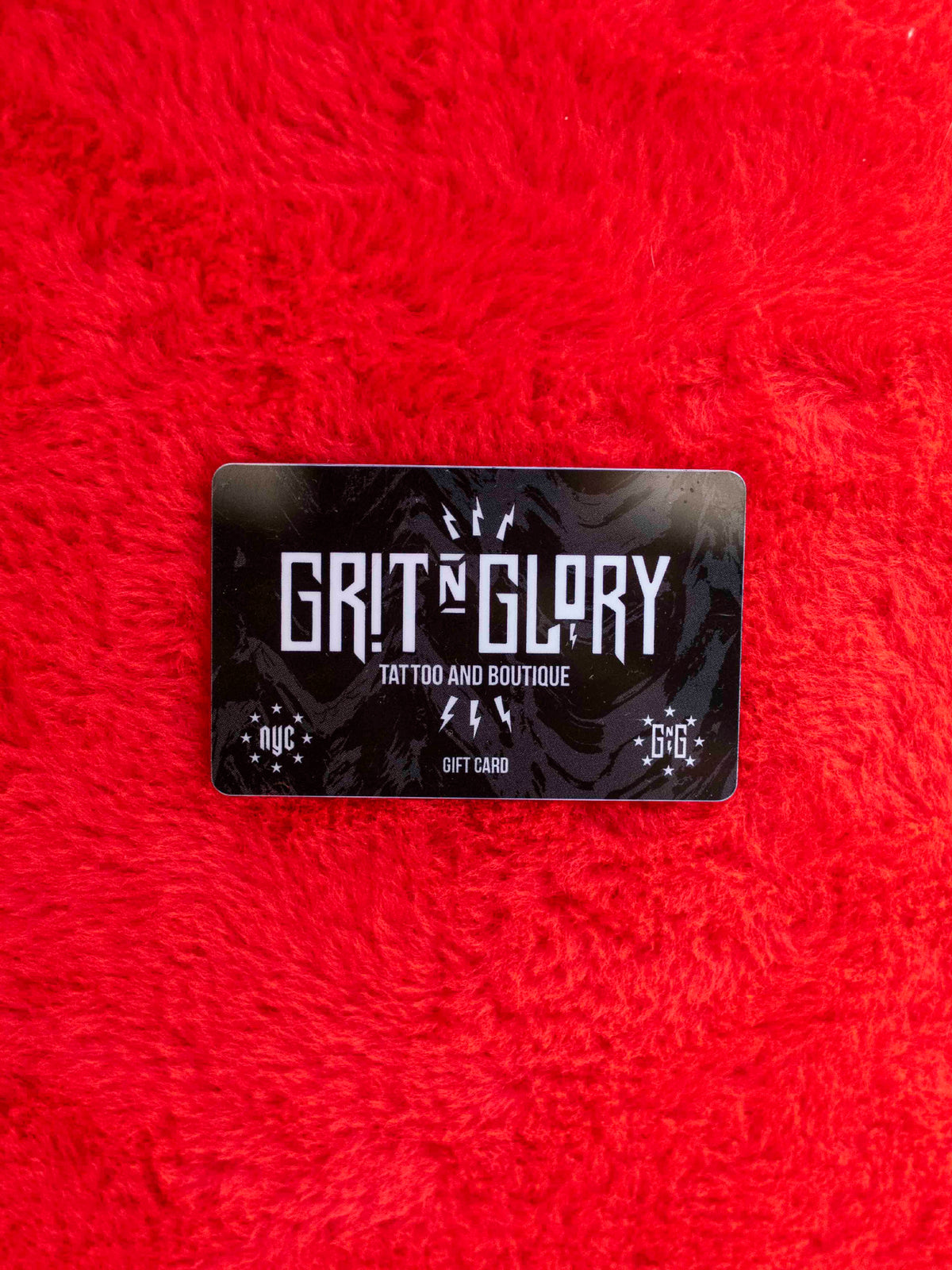 Grit N Glory gift card in black white and gray on a fuzzy red background. 