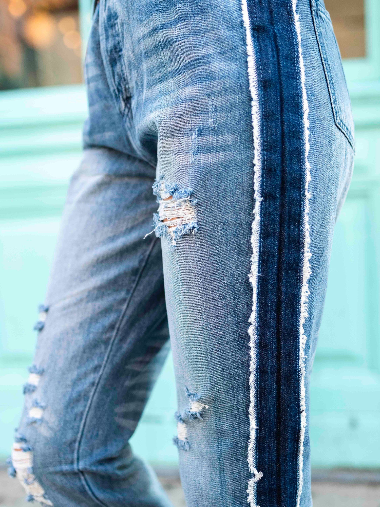 A person wearing a black crop top and blue, two-toned rolled boyfriend jeans with a frayed hem, standing in front of a teal-colored building.