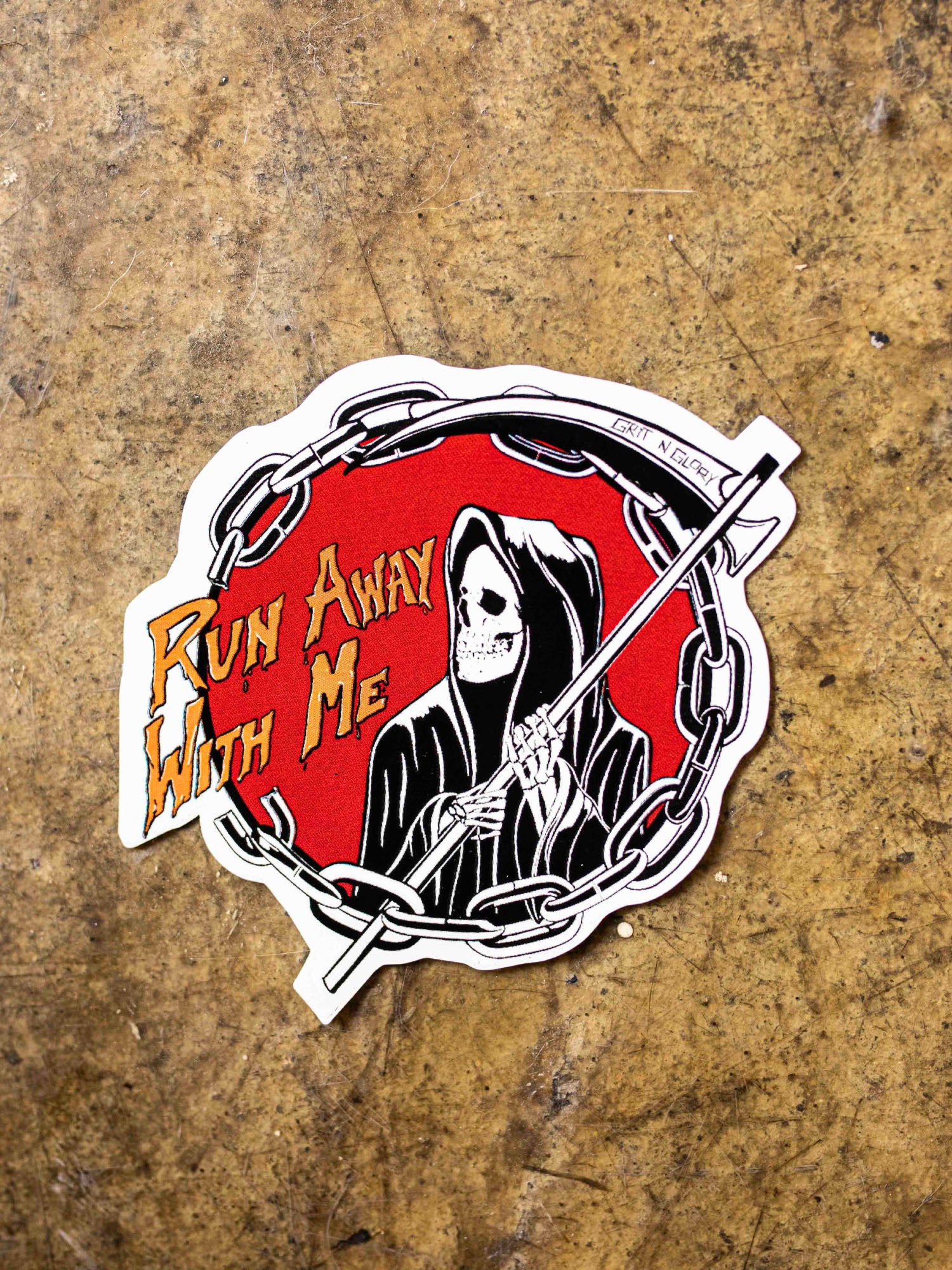 A die cut vinyl sticker with a black and white reaper design in a red circle.