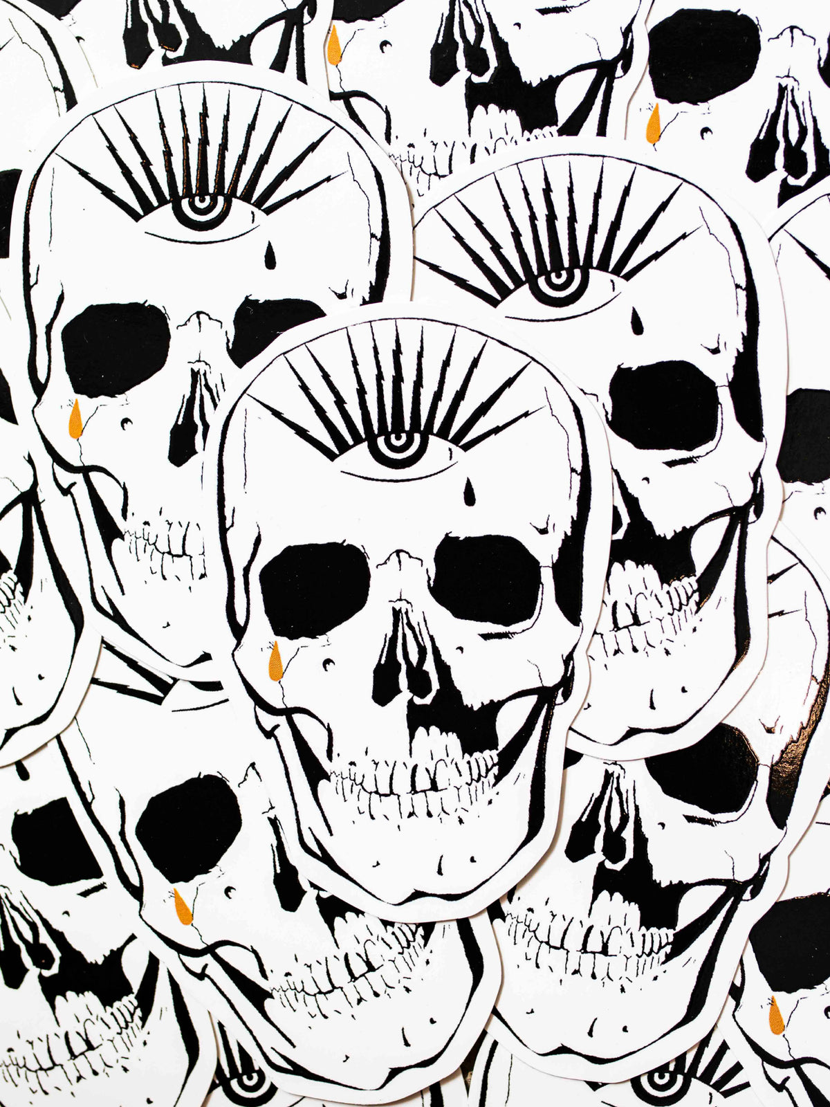 A black, white, and gold die-cut sticker of a skull with an eye the top forehead area.