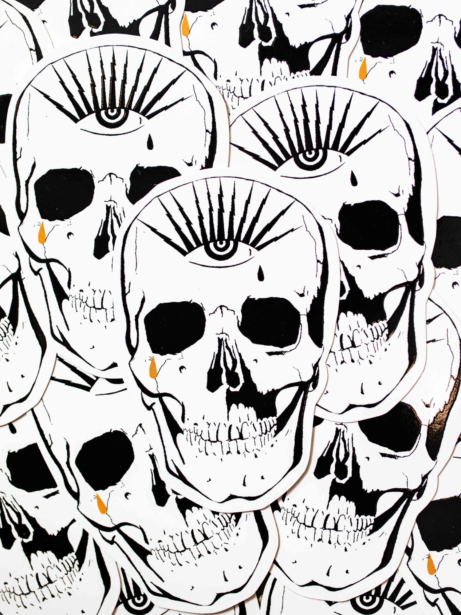 A black, white, and gold die-cut sticker of a skull with an eye the top forehead area.