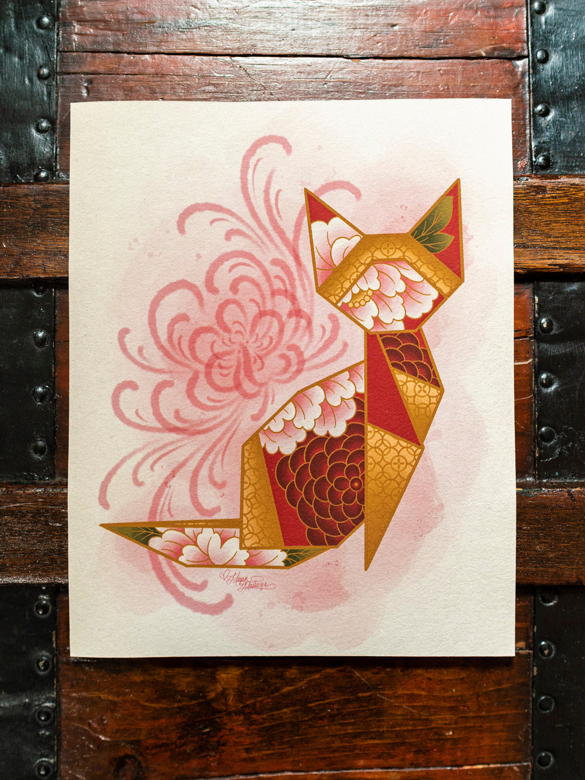 Red and gold origami cat with floral patterns on a wooden surface.