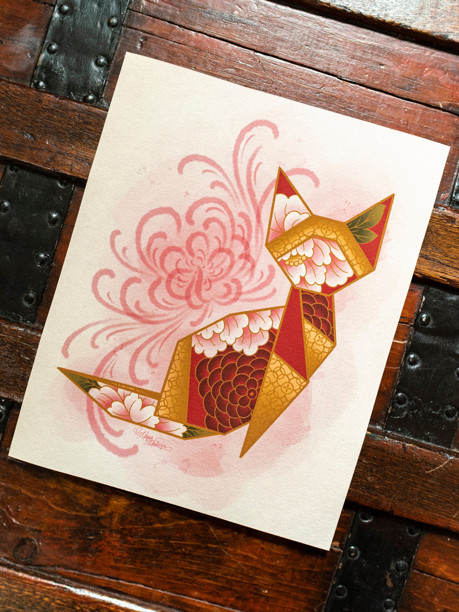 Red and gold origami cat with floral patterns on a wooden surface.