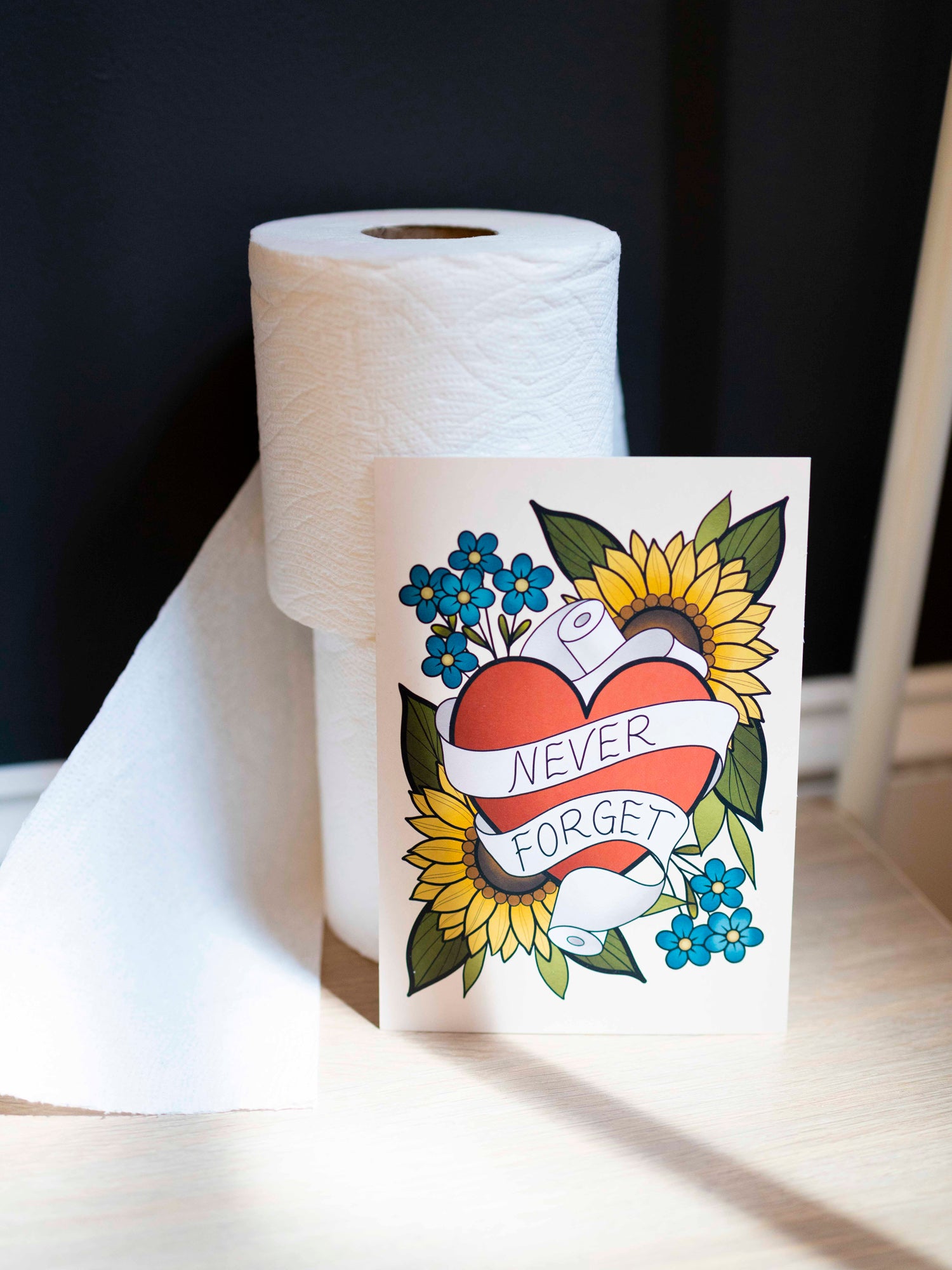 Small funny art print reads "never forget" in a traditional tattoo style leaning against toilet paper rolls.