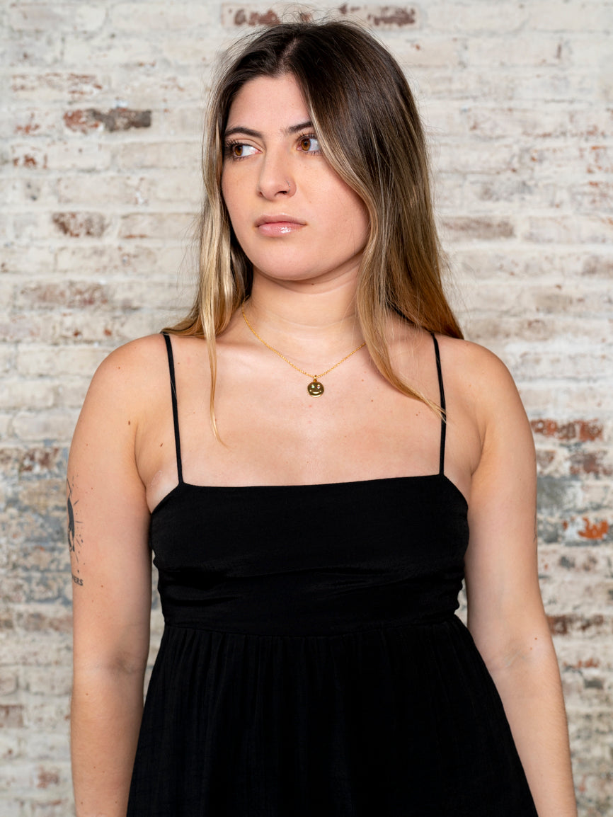 model wearing a black cami strapped dress with classic converse style sneakers against a rustic brick wall. 