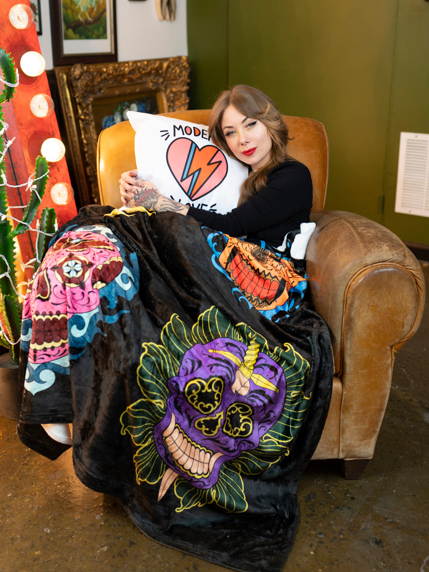Megan Massacre with her black and white plush blanket with a colorful sugar skull design on a chair.