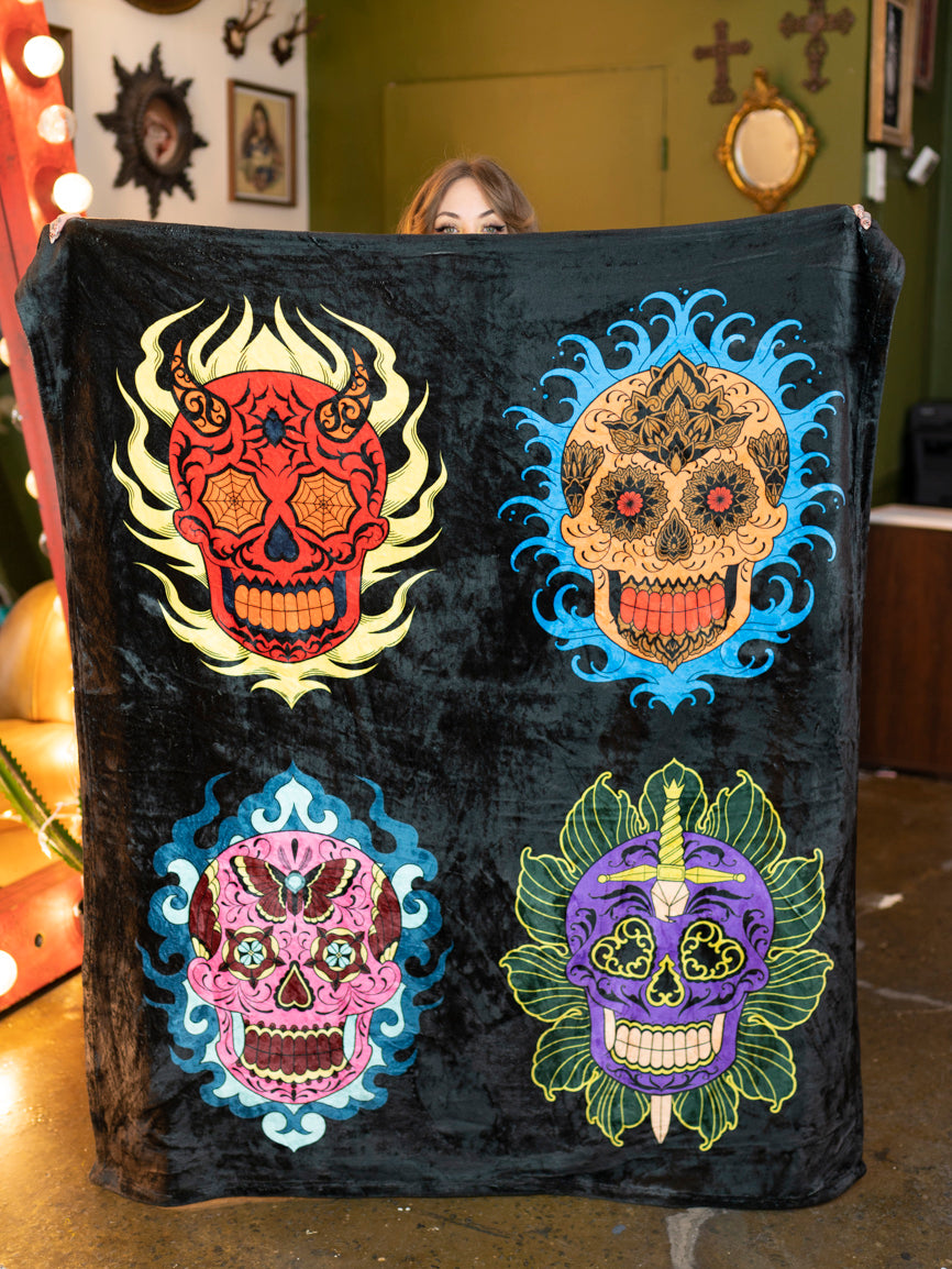 A black and white plush blanket with a colorful sugar skull design displayed on a chair.