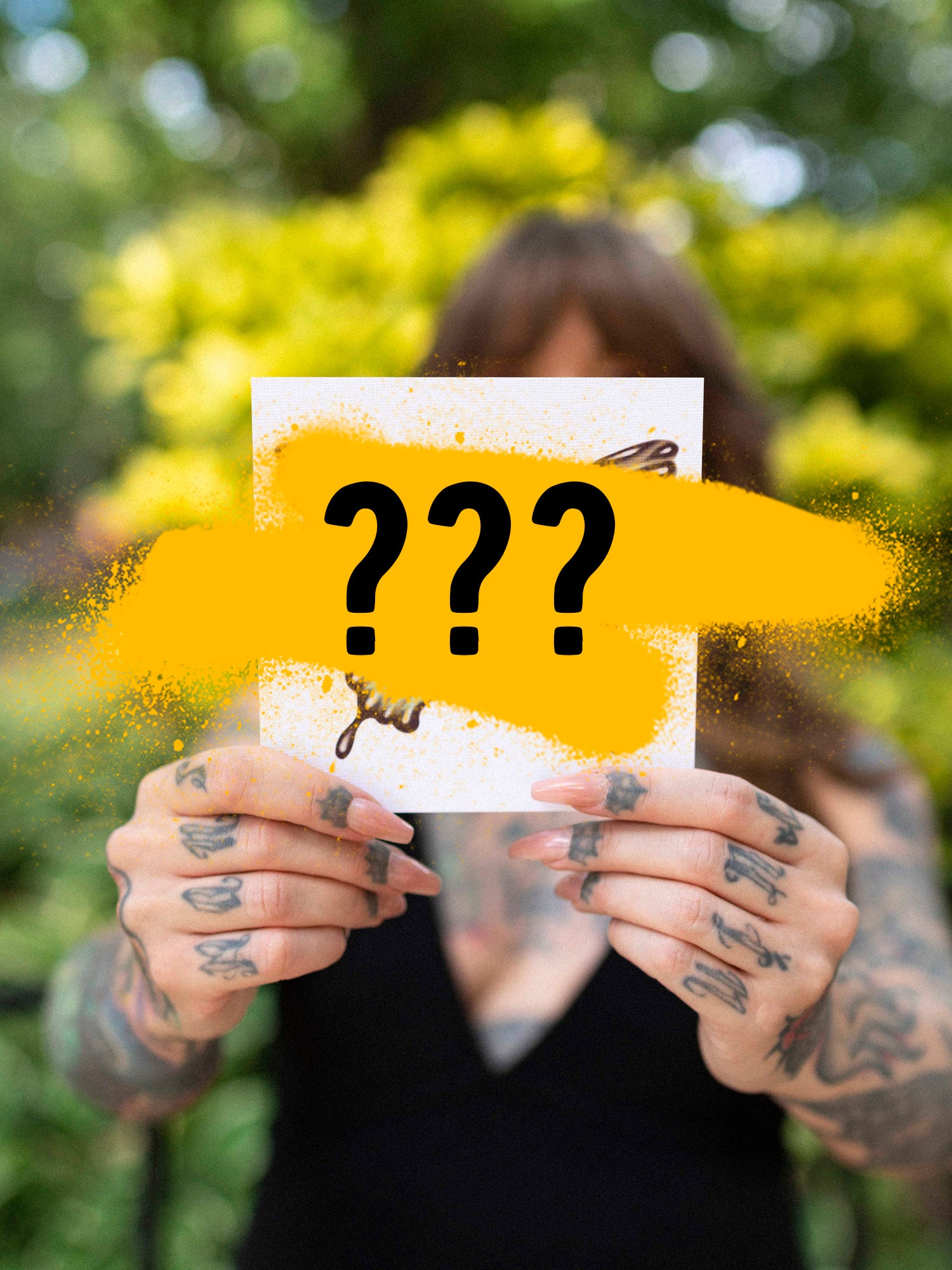 A person holding a mystery print with yellow and black design elements, partially covering the image with their hands.