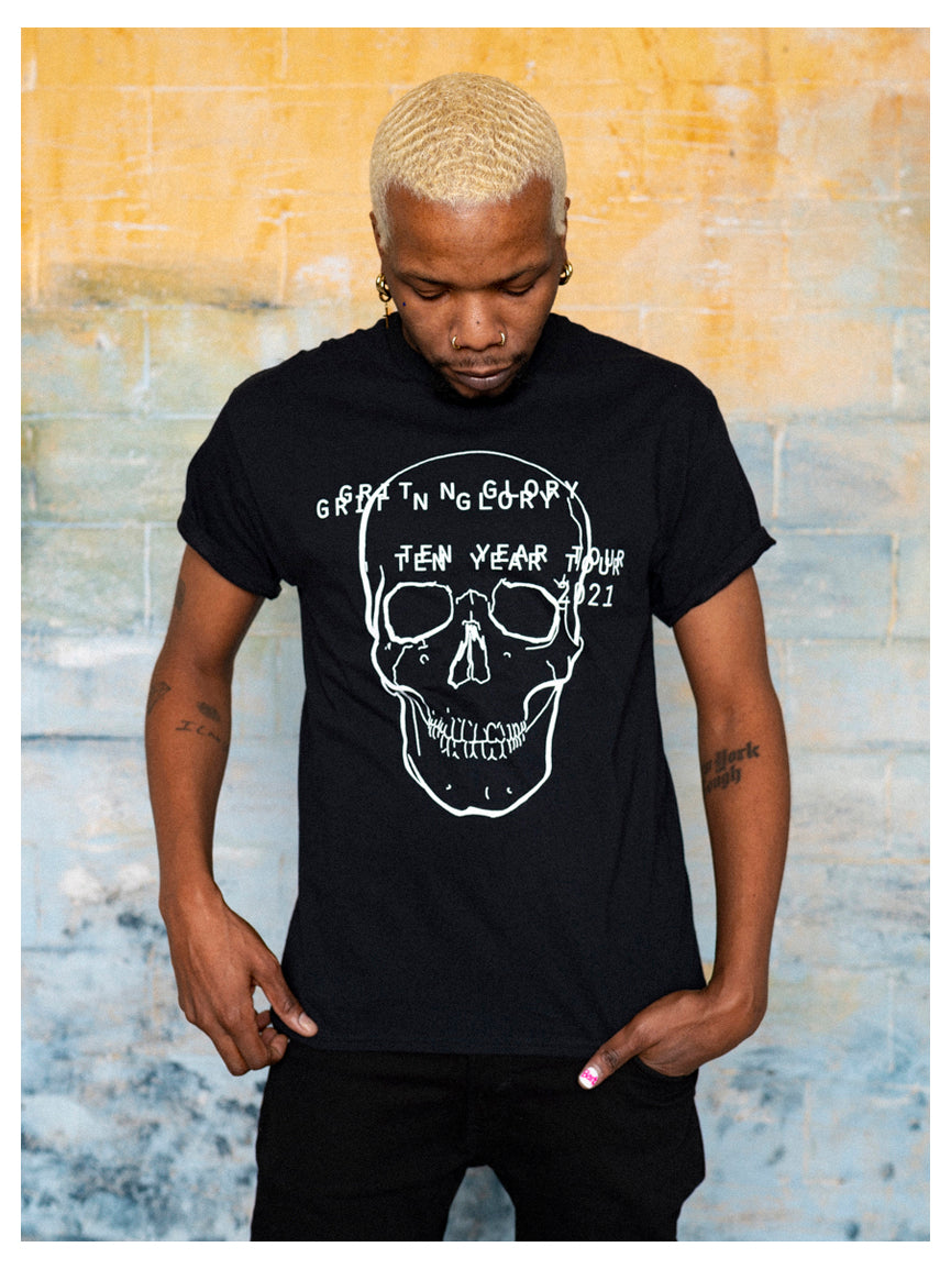 A person wearing a black graphic t-shirt with a white text and skull design on it. Text reads "Grit N Glory Ten Year Tour 2021" in a doubled font.