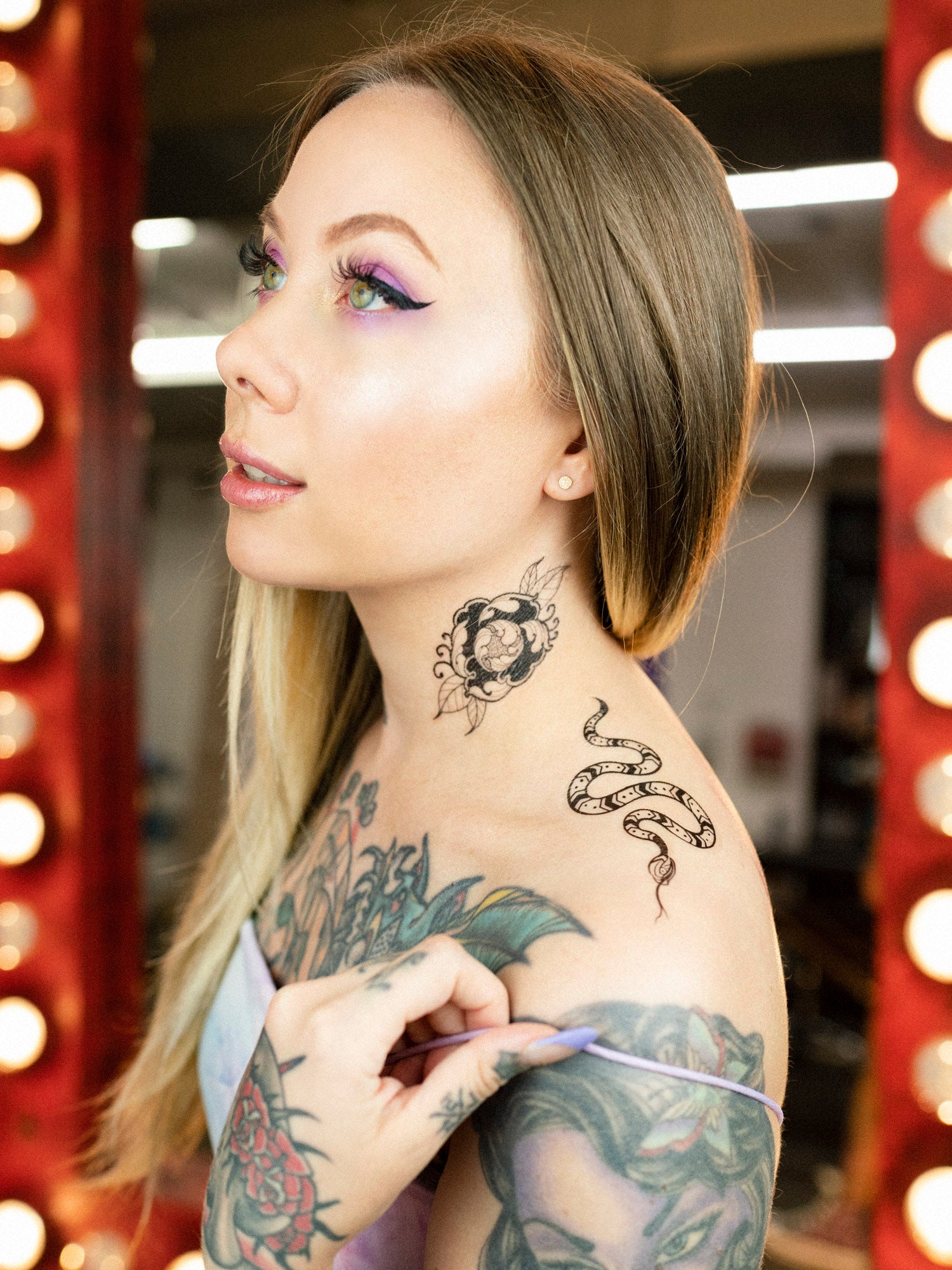 Temporary tattoos with a fine line flower and snake design, accompanied by a shine remover, displayed on a leafy background.