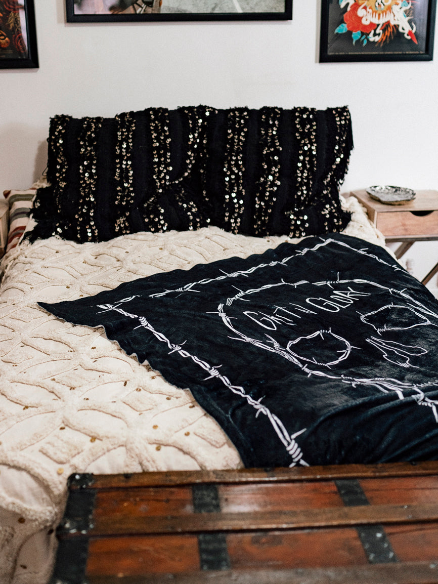 A black blanket with a white skull design and the text 'GRIT N GLORY' on a bed.