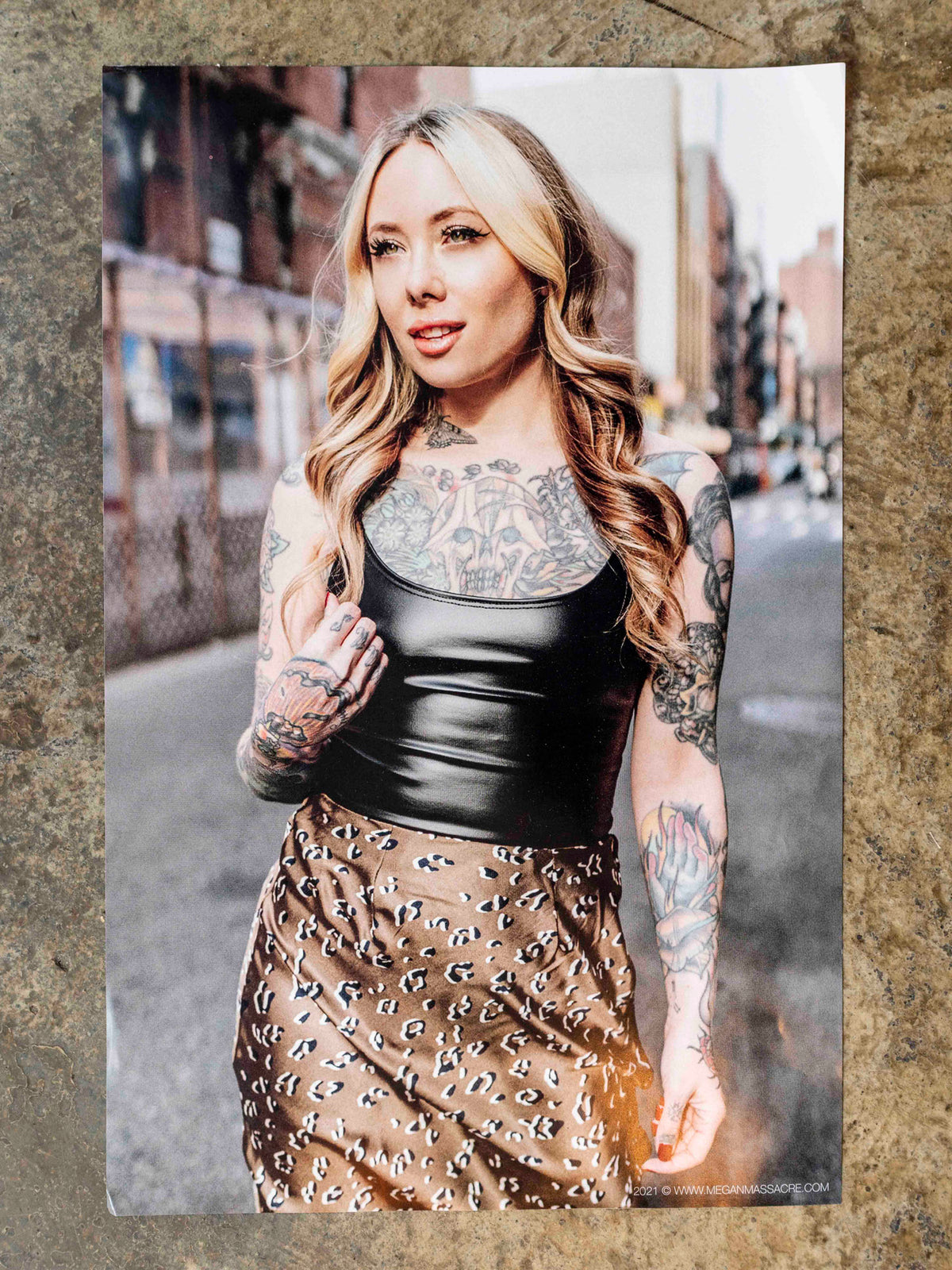 Poster of tattoo artist Megan Massacre with blonde hair with black top and chetah skirt photographed in the lower east side nyc. 