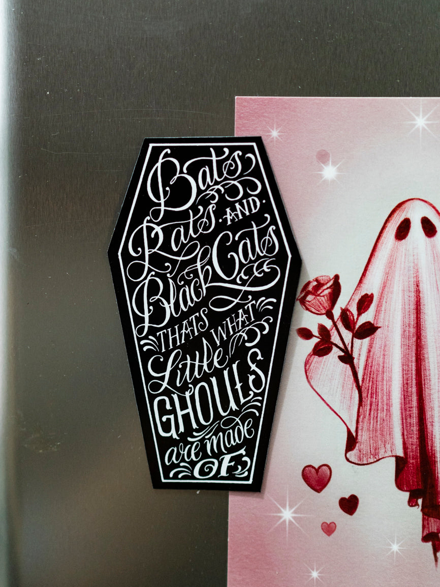 A black and white magnet with a coffin shape featuring the phrase 'Bats, rats and black cats. That's what little ghouls are made of' in a white, stylized font.
