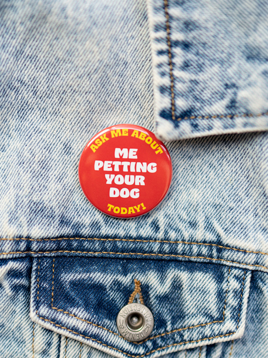 A red and yellow pin with text 'ASK ME ABOUT PETTING YOUR DOG TODAY' attached to a blue denim jacket.