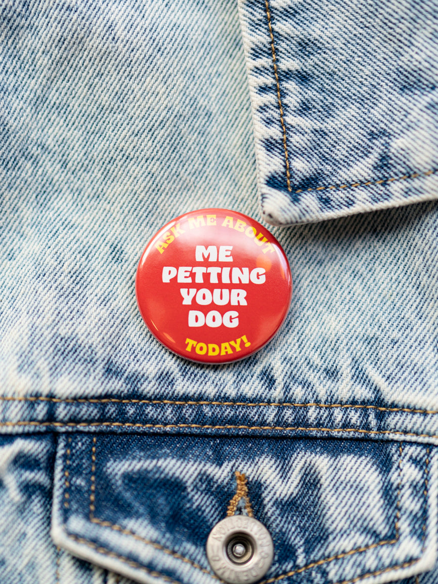 A red and yellow pin with text 'ASK ME ABOUT PETTING YOUR DOG TODAY' attached to a blue denim jacket.
