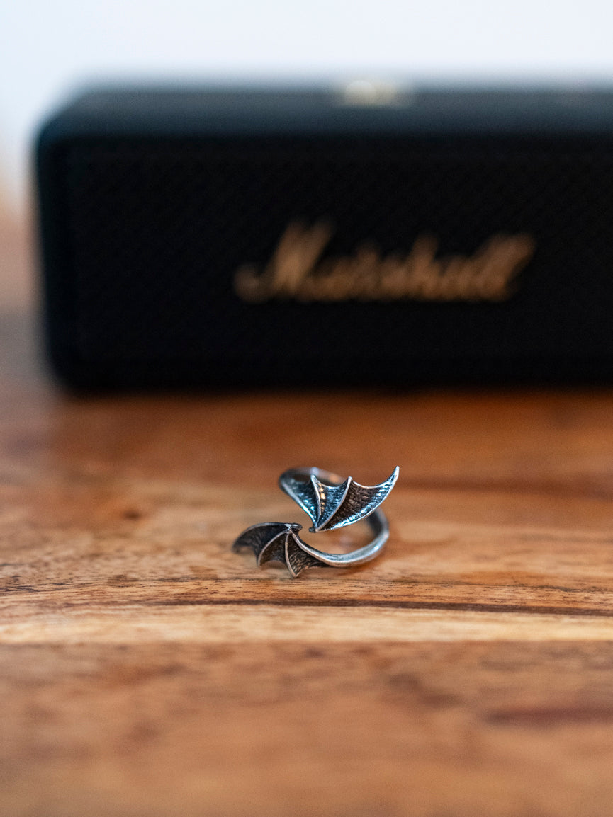 A pewter bat wing wrap around ring displayed on a wooden surface with a Marshall amplifier in the background.
