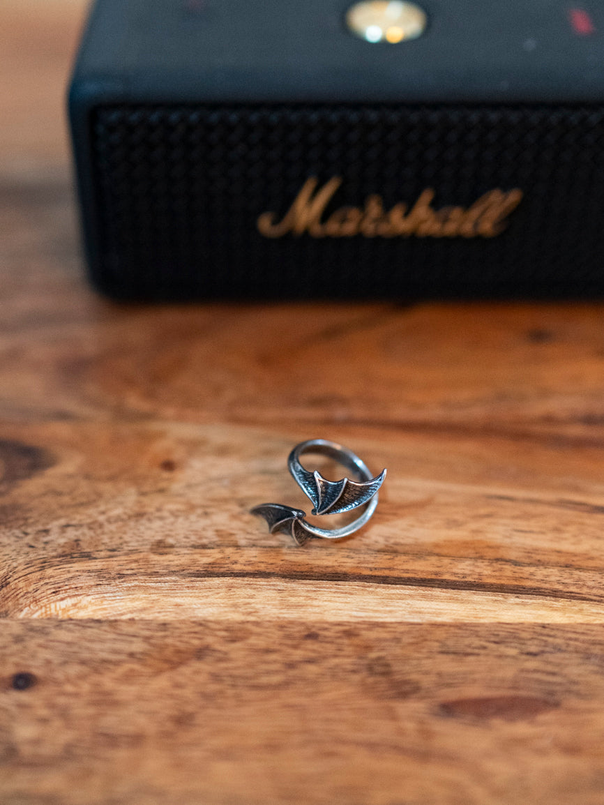 A pewter bat wing wrap around ring displayed on a wooden surface with a Marshall amplifier in the background.