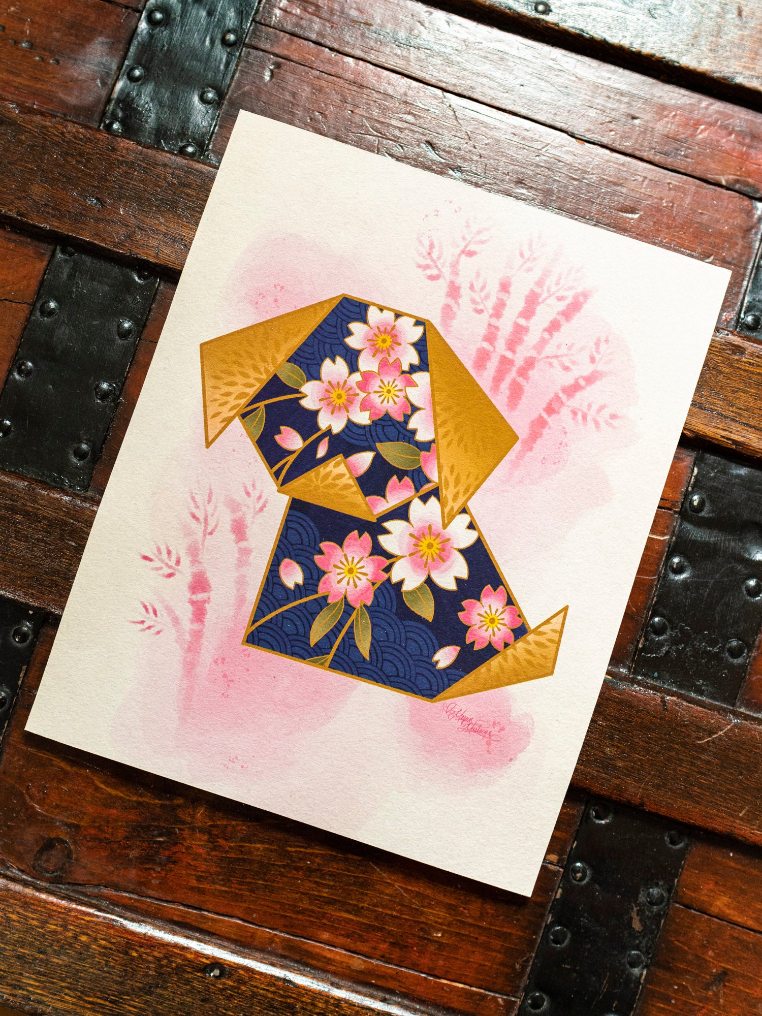 An origami dog print by Megan Massacre on archival watercolor paper, displayed on a wooden surface.