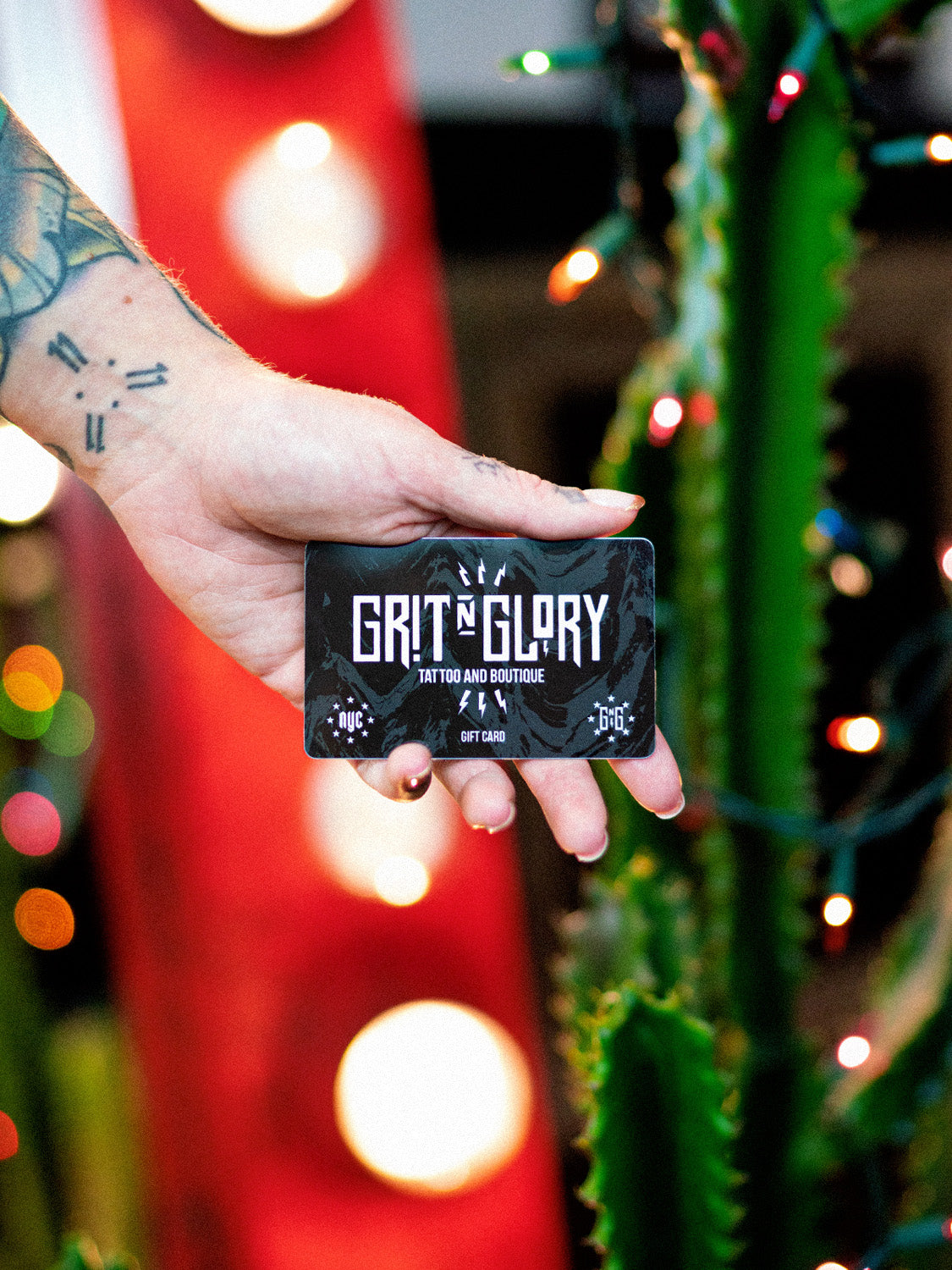 Hand holding black and white Grit N Glory gift card in front of a mirror and green cactus
