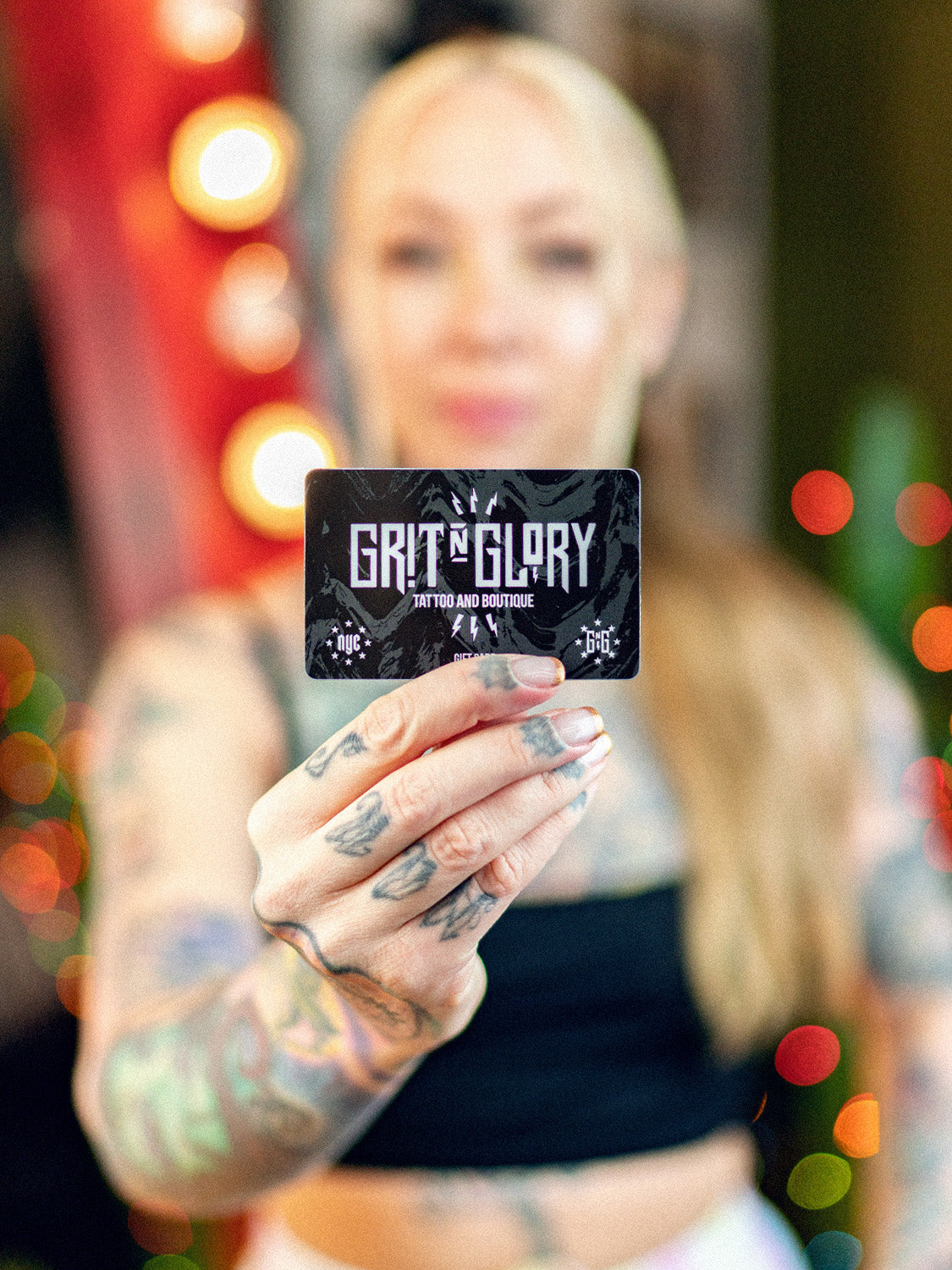 Hand holding black and white Grit N Glory gift card in front of a mirror and green cactus