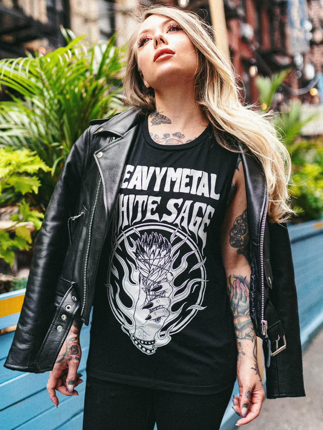 Megan Massacre standing on the sidewalk wearing a black leather cropped moto jacket with a sleeveless top underneath.