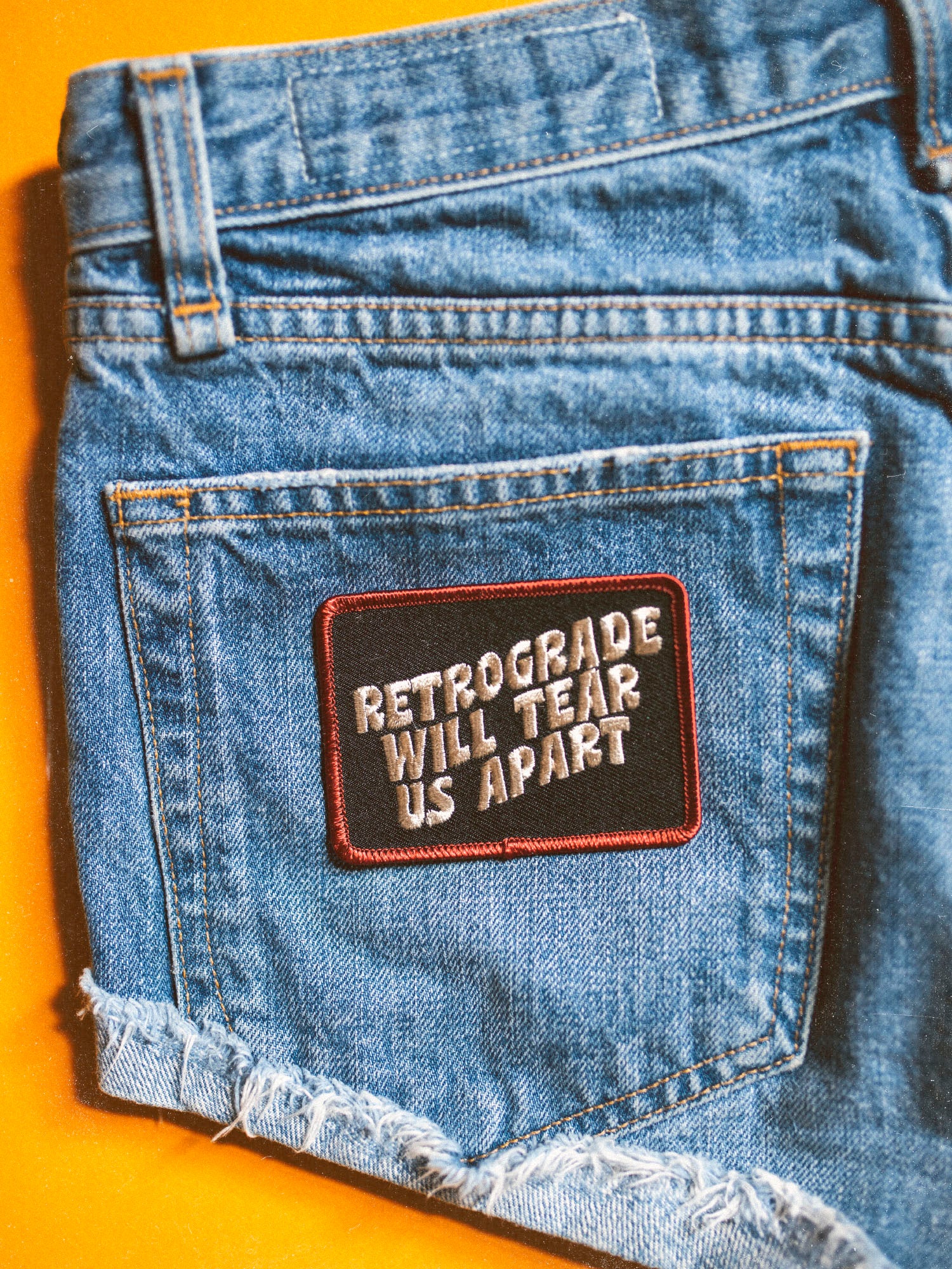 A canvas embroidered patch with text 'RETROGRADE WILL TEAR US APART' ironed onto a denim fabric.