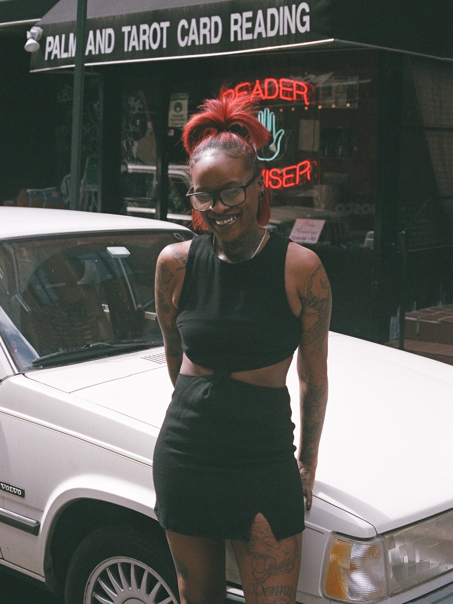 A person standing beside a car wearing a black mini dress with cutouts and a small front slit.