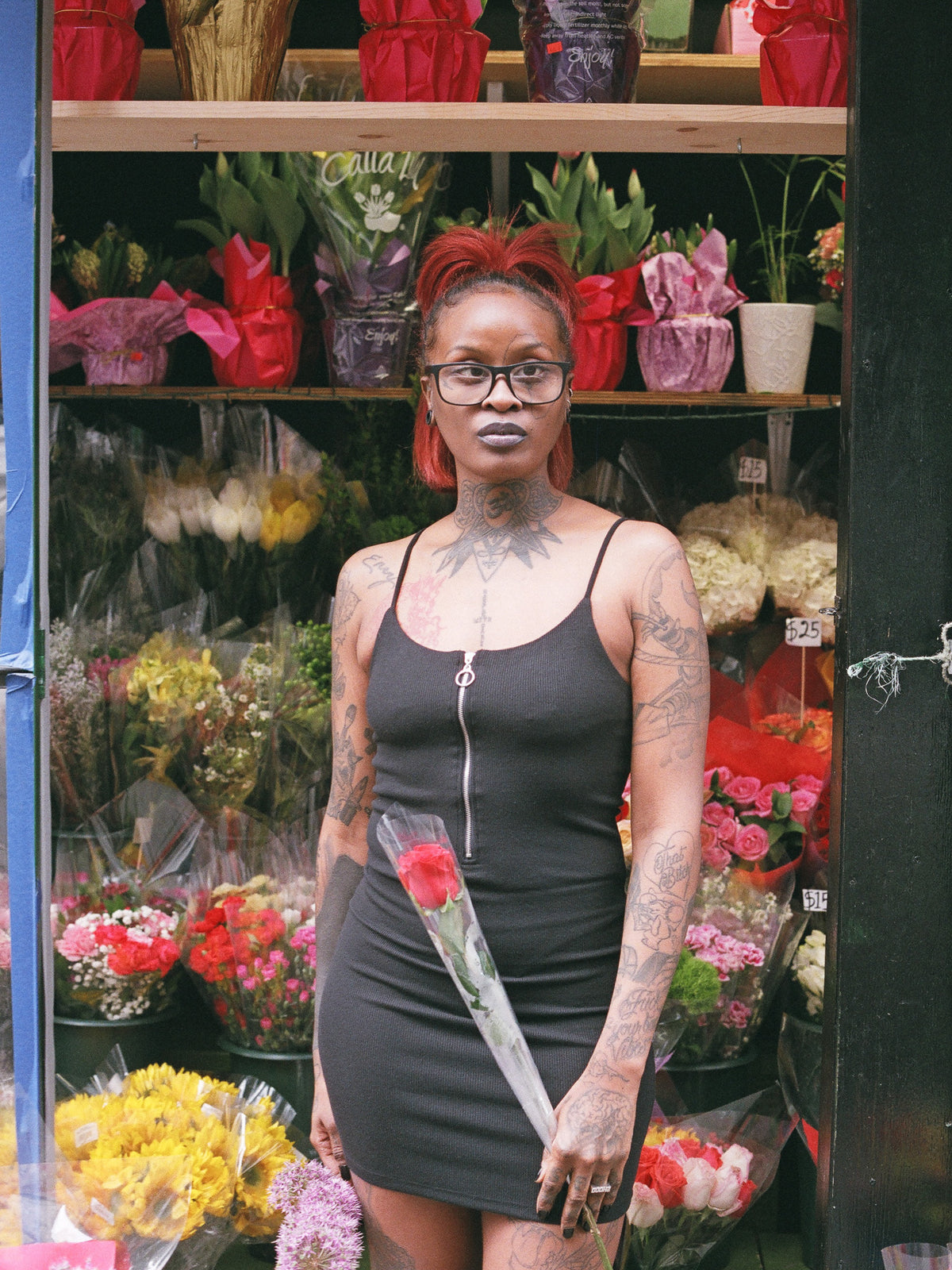 A person wearing a black zip up, cami strapped mini dress in front of a flower stall. 