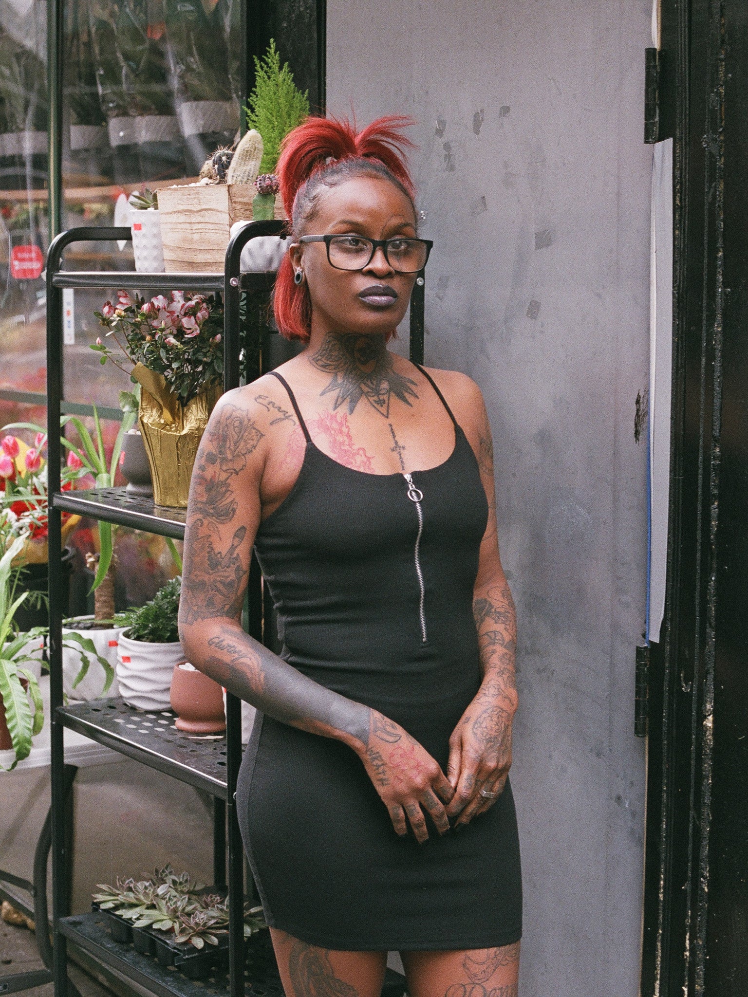 Model with red hair and glasses wearing the "As She Was Mini Dress," a stylish and versatile black mini dress. The dress is designed with a sleek front zipper detail, adding a touch of edginess to the rib knit fabric which ensures both comfort and flexibility.