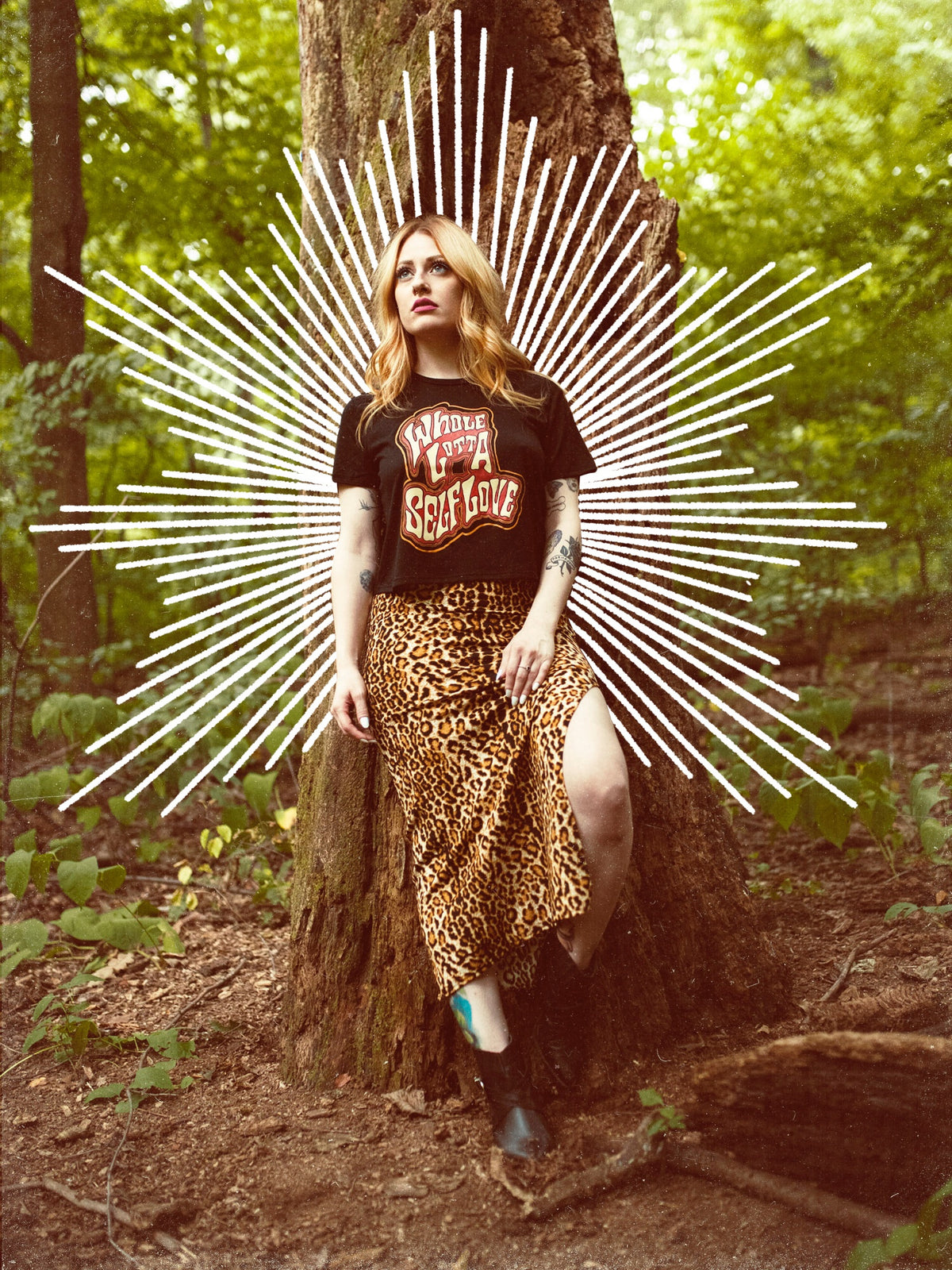 A female model wearing a black crop top with the graphic 'Whole Lotta Self Love' and a maxi style skirt standing next to a tree.