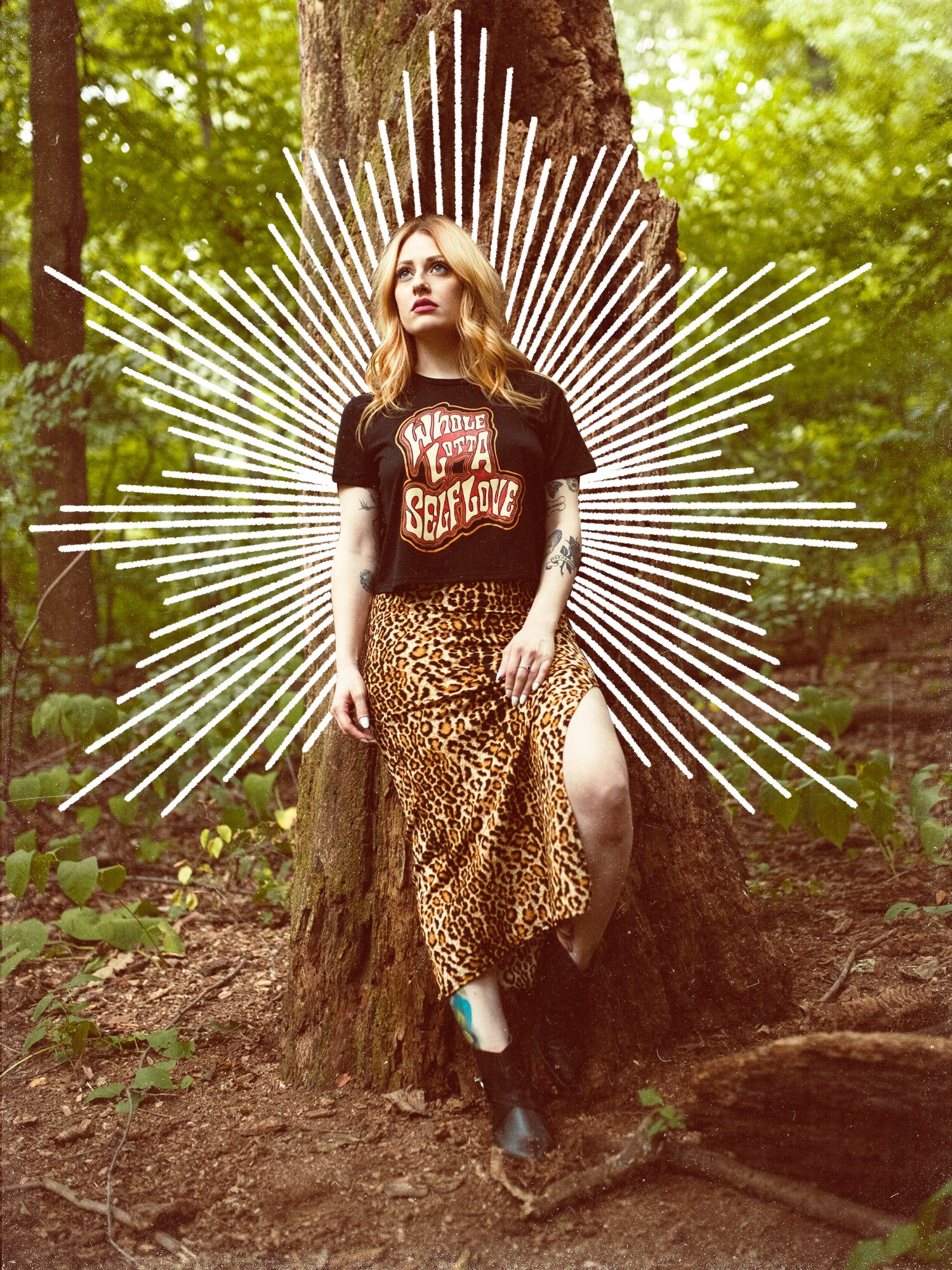 A female model wearing a black crop top with the graphic 'Whole Lotta Self Love' and a maxi style skirt standing next to a tree.