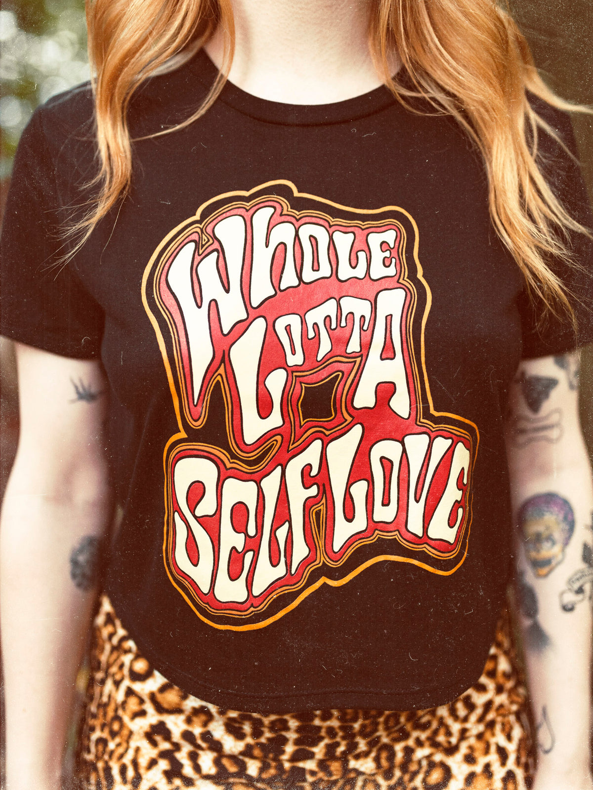 Close up of the Whole Lotta Self Love black crop top featuring a red, orange, and cream text graphic. 