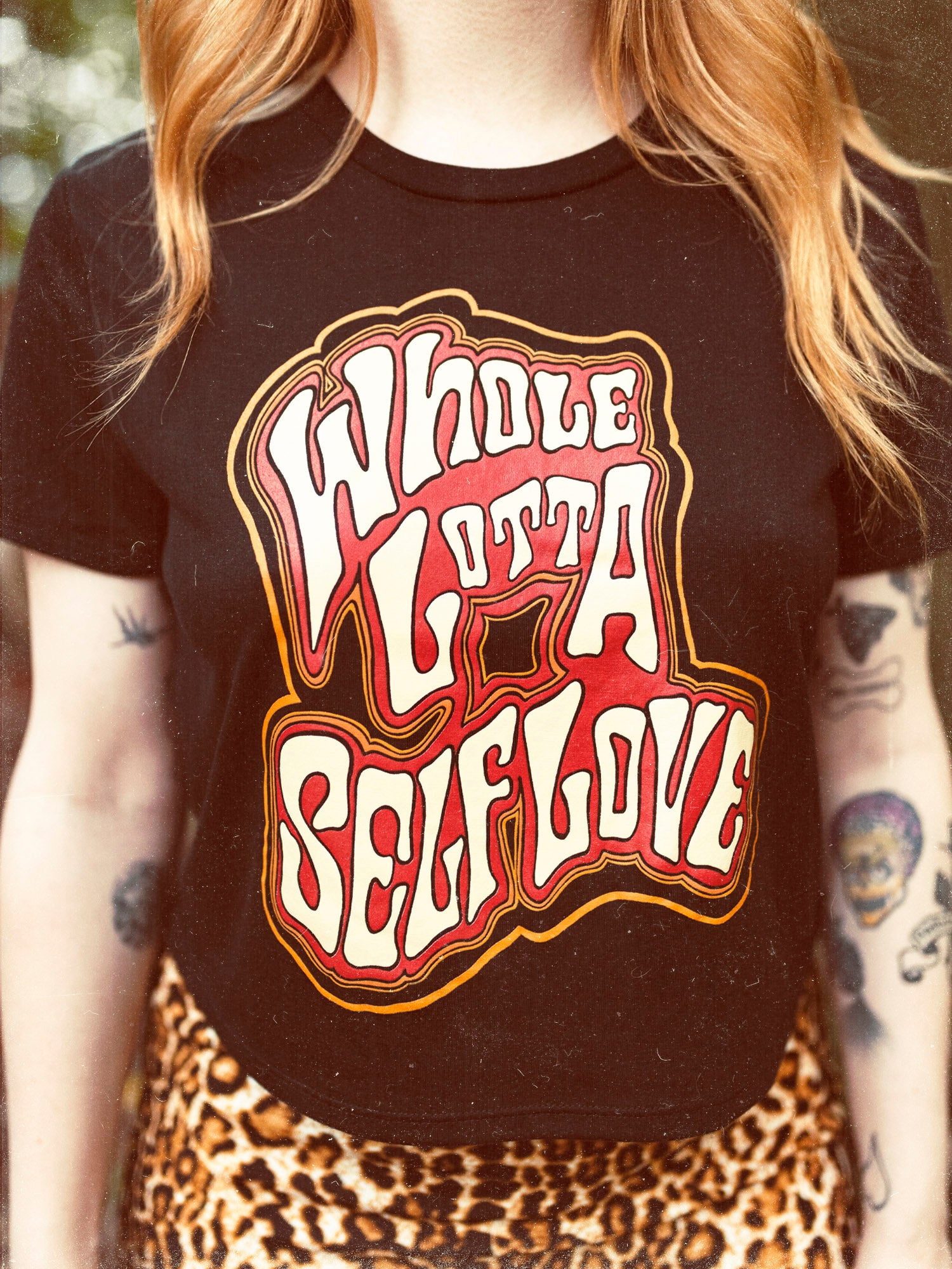 Close up of the Whole Lotta Self Love black crop top featuring a red, orange, and cream text graphic. 
