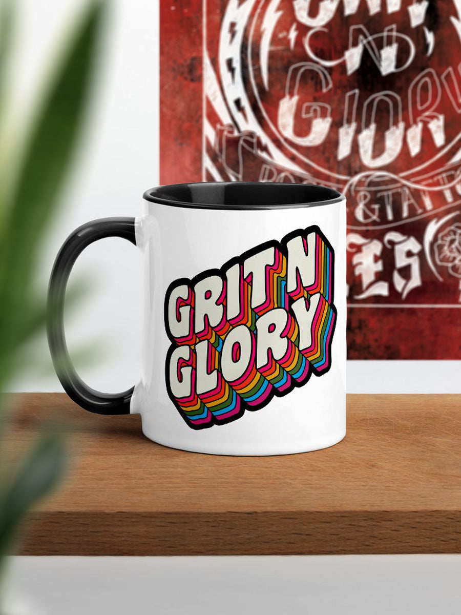 A white and black ceramic mug with a colorful 'Grit N Glory' logo print.